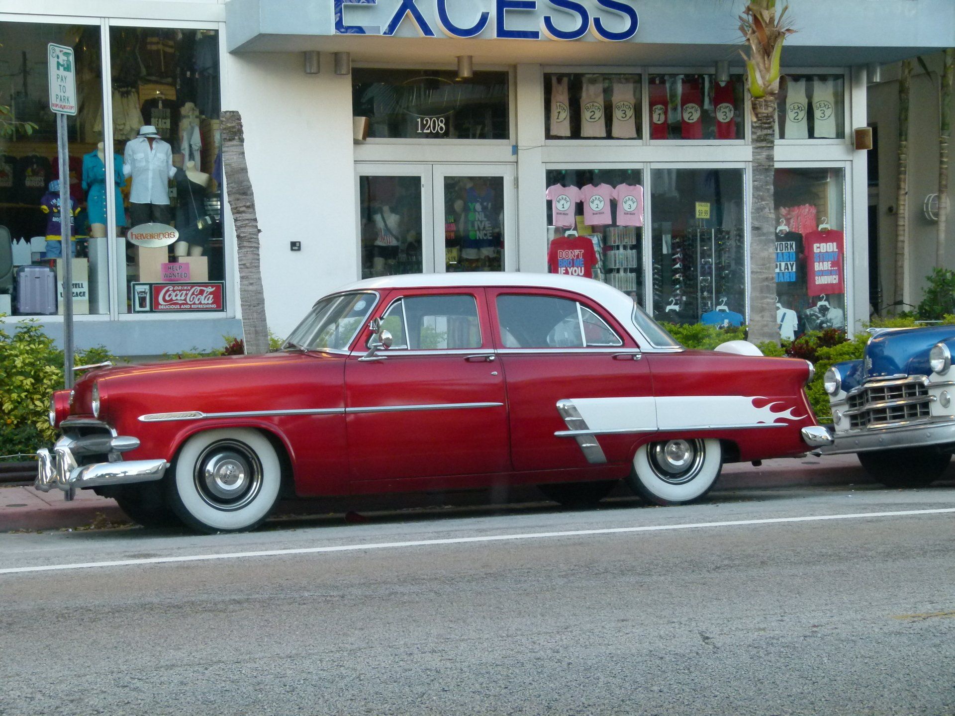 A red car is parked in front of a store called excess