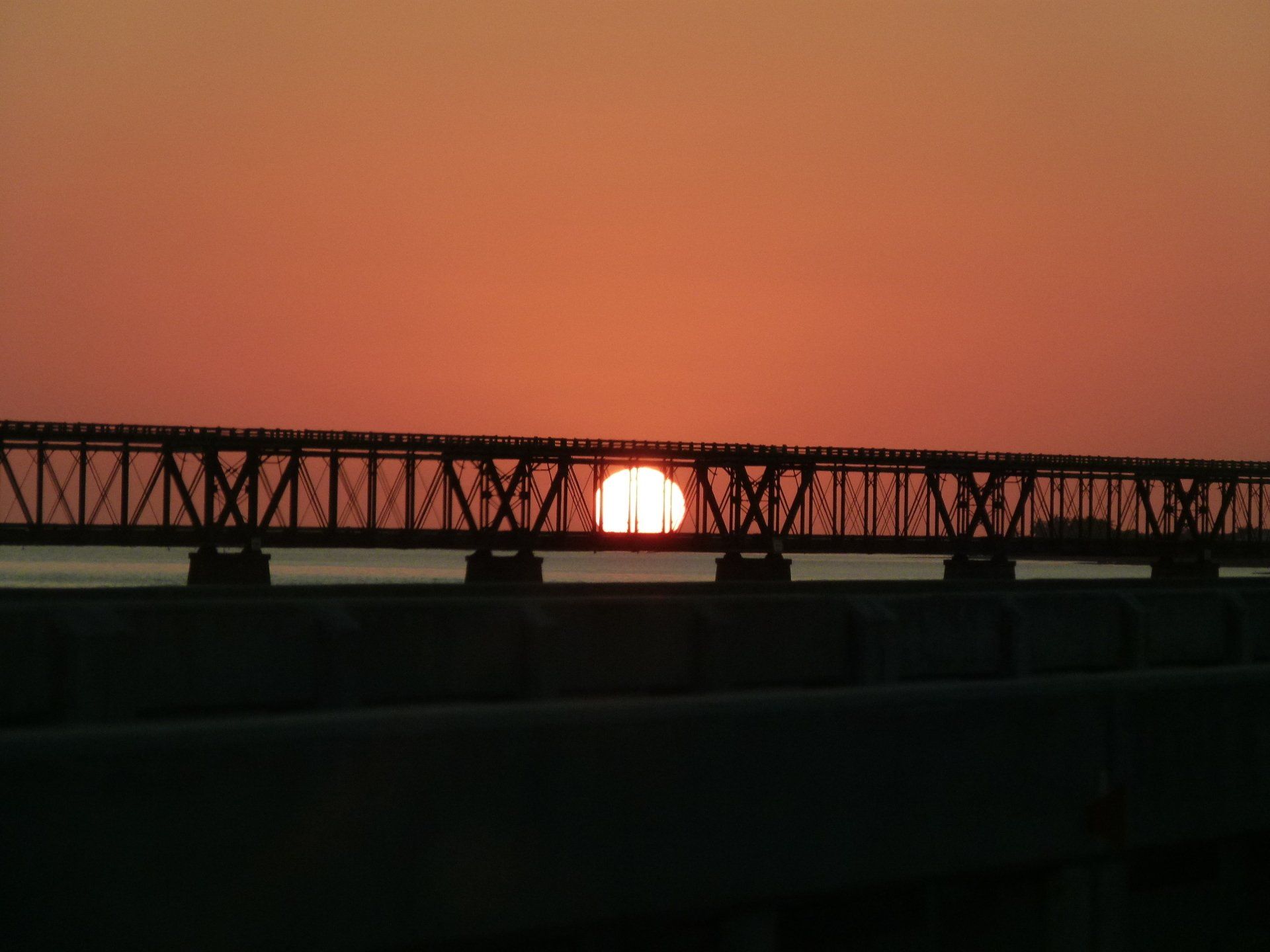 The sun is setting behind a bridge over a body of water