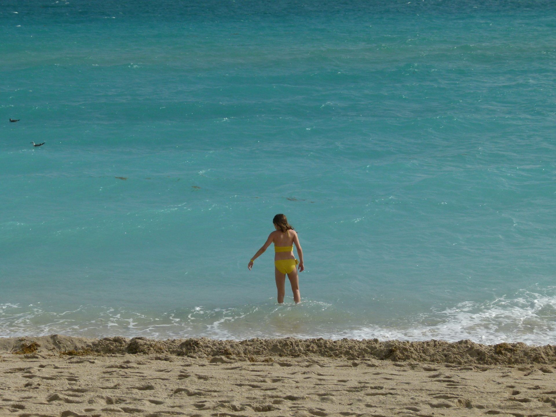 A woman in a yellow bikini is standing in the ocean.