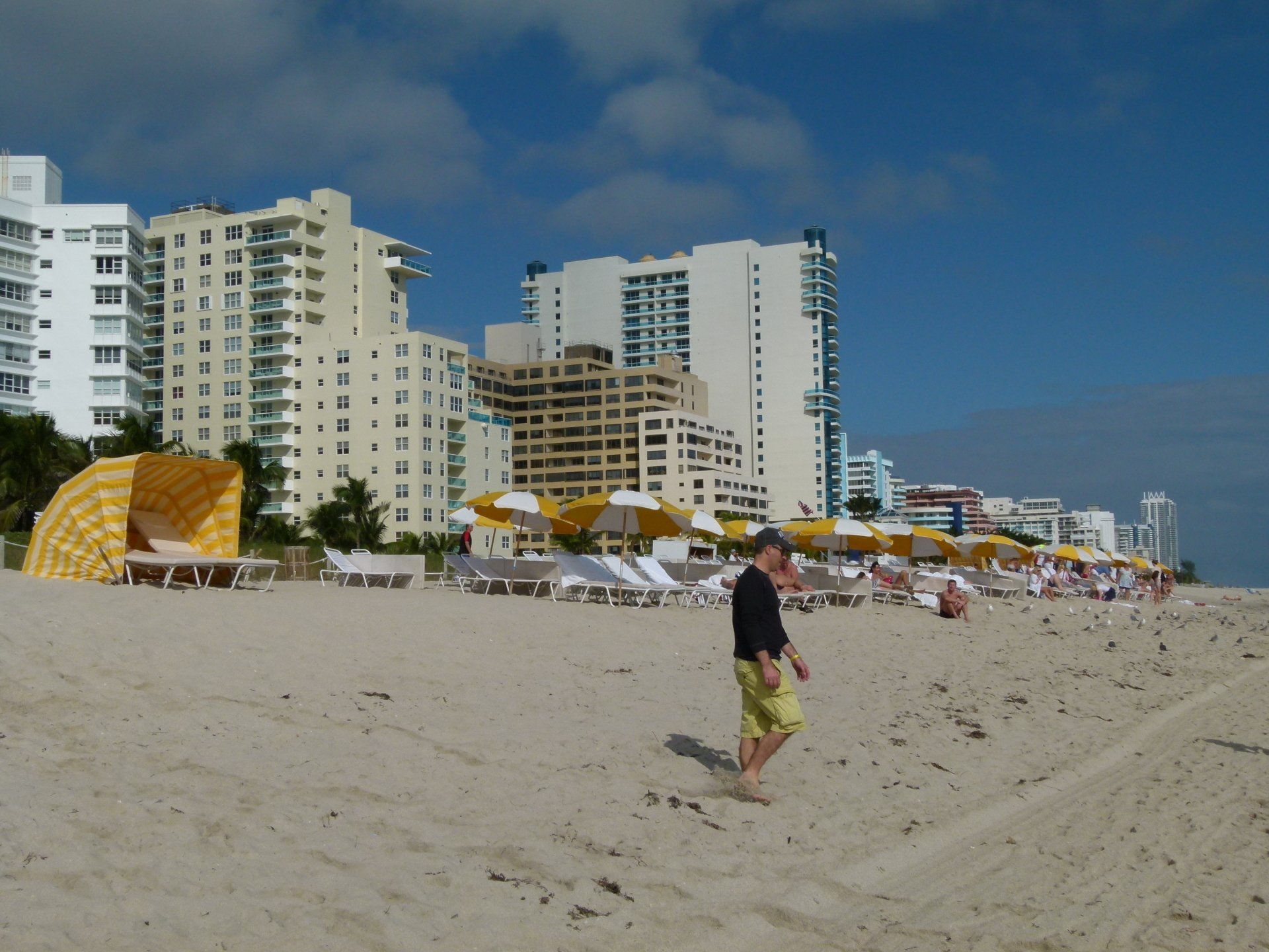 A man walking on a beach with tall buildings in the background