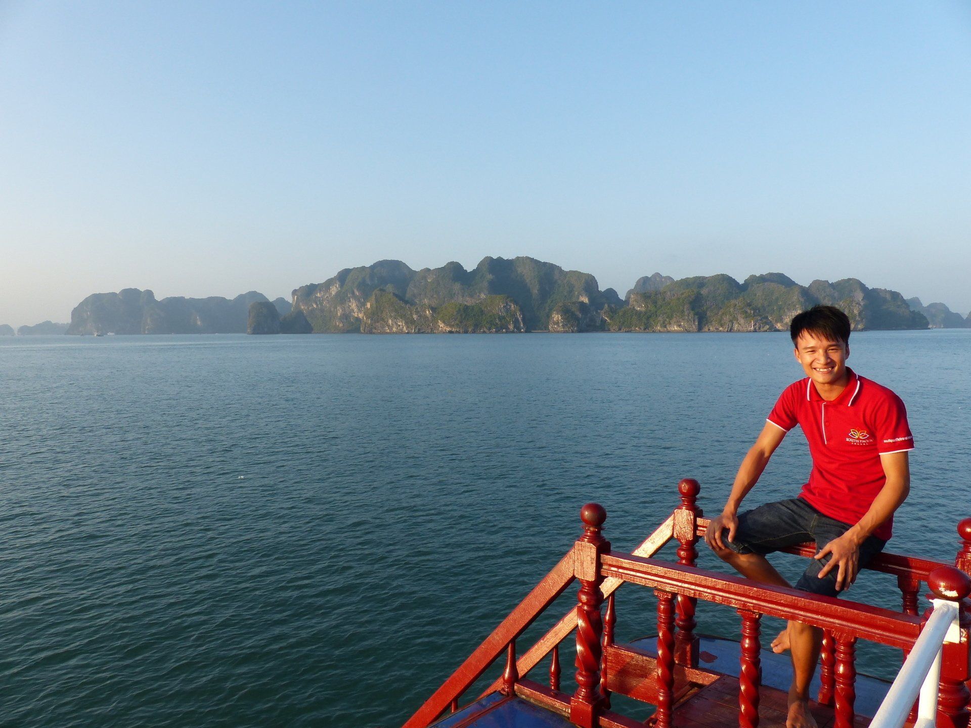 A man in a red shirt is sitting on the deck of a boat overlooking the ocean.