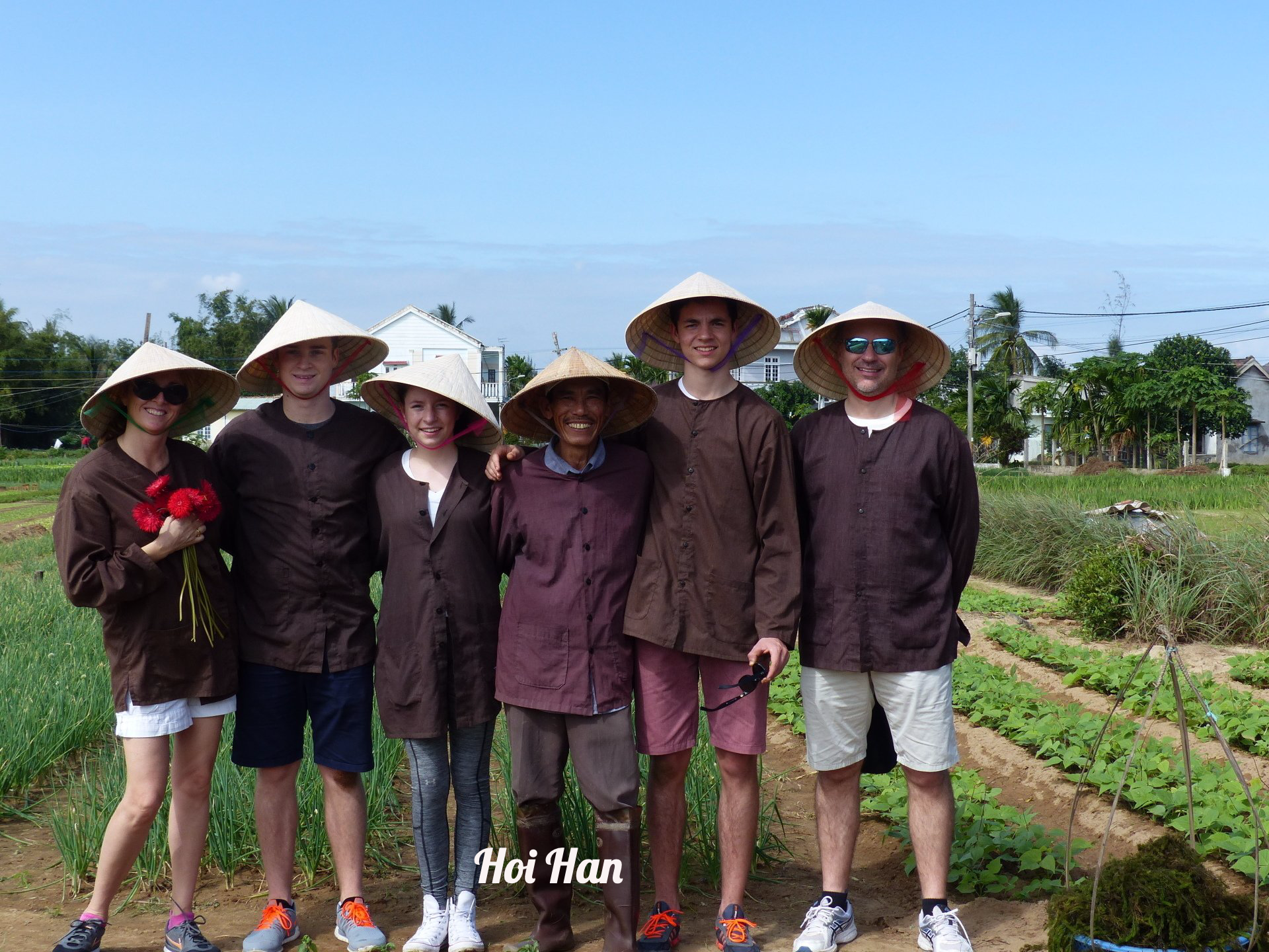 A group of people wearing conical hats are posing for a picture in a field.