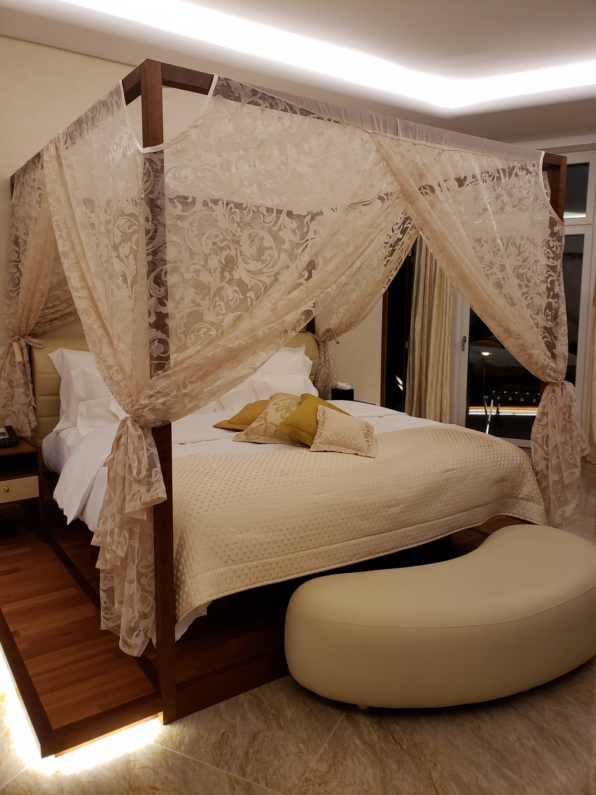 A bedroom with a canopy bed and a white ottoman