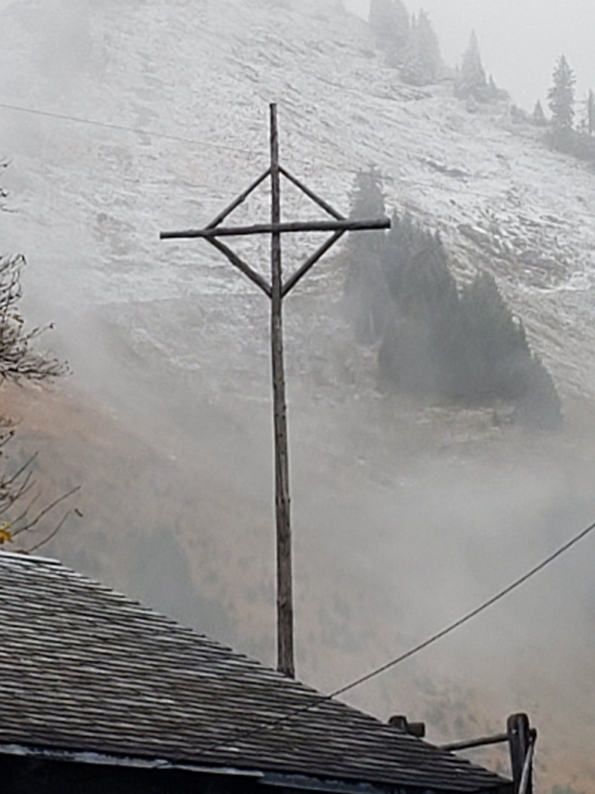 A cross is sitting on top of a wooden pole in front of a snowy mountain.