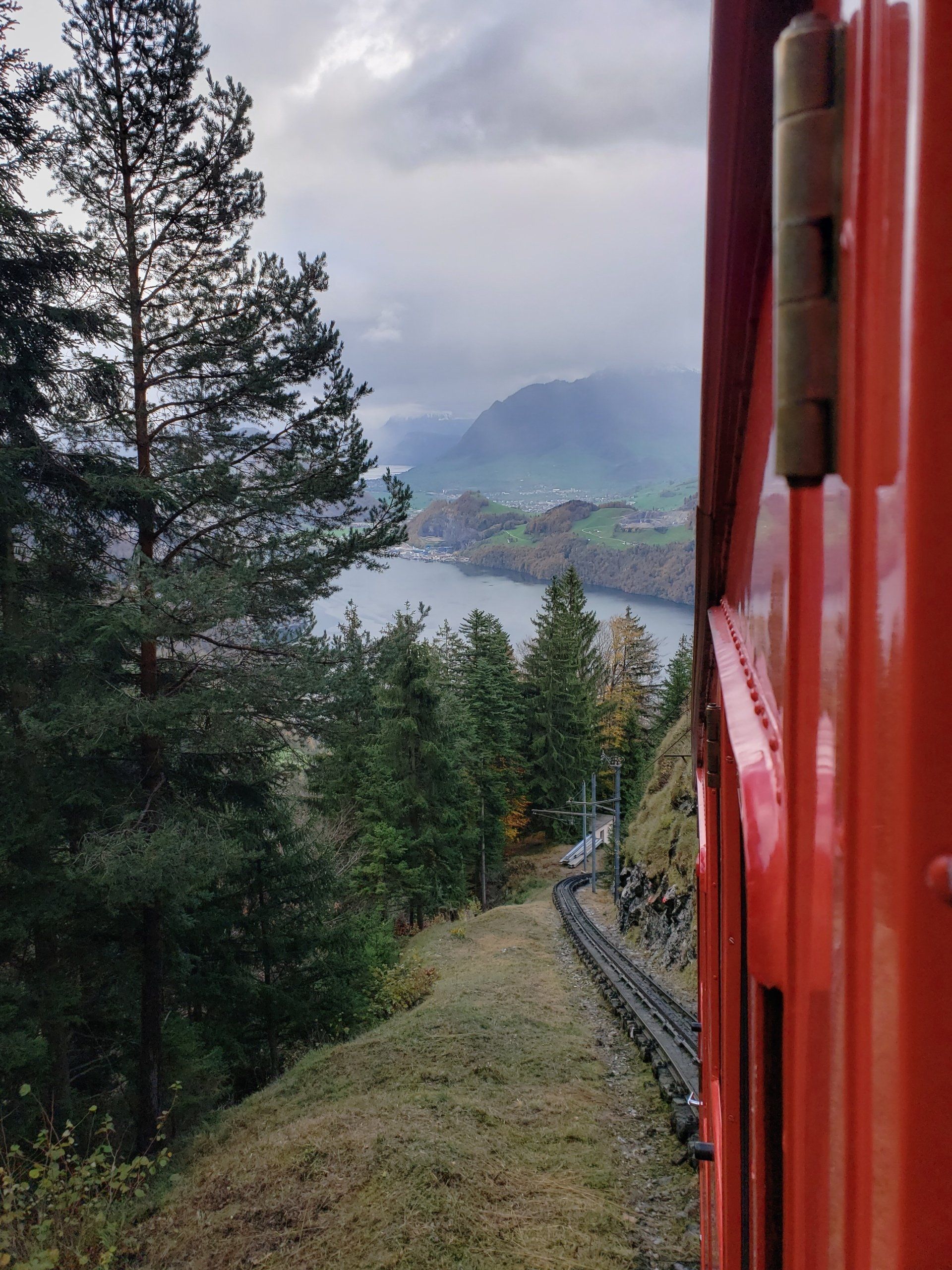 A red train is going down a hill with trees and mountains in the background