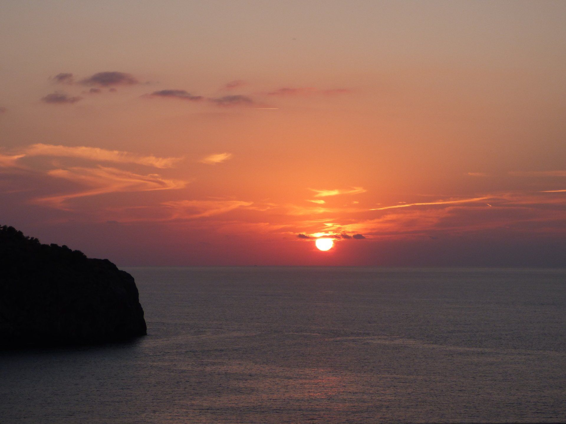 A sunset over the ocean with a cliff in the foreground