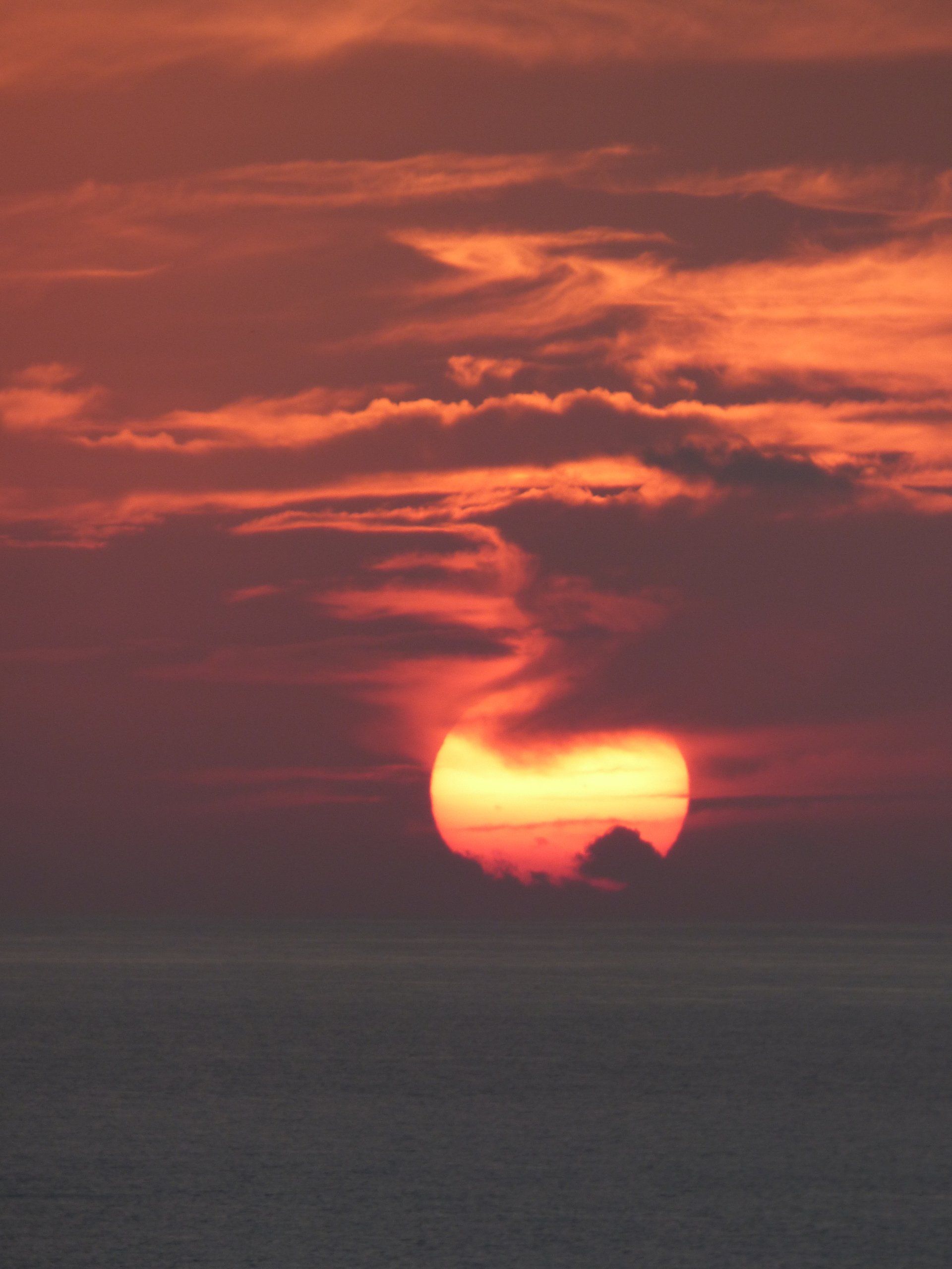 A sunset over the ocean with the sun shining through the clouds