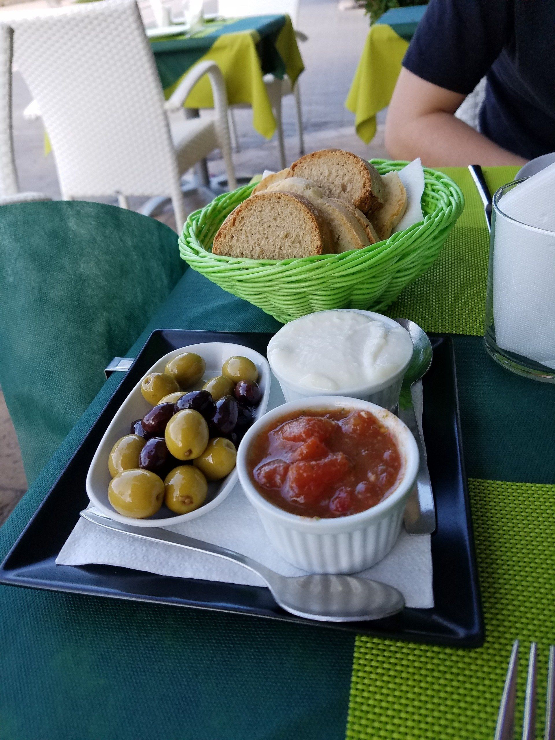 A person is sitting at a table with a basket of bread and a tray of food