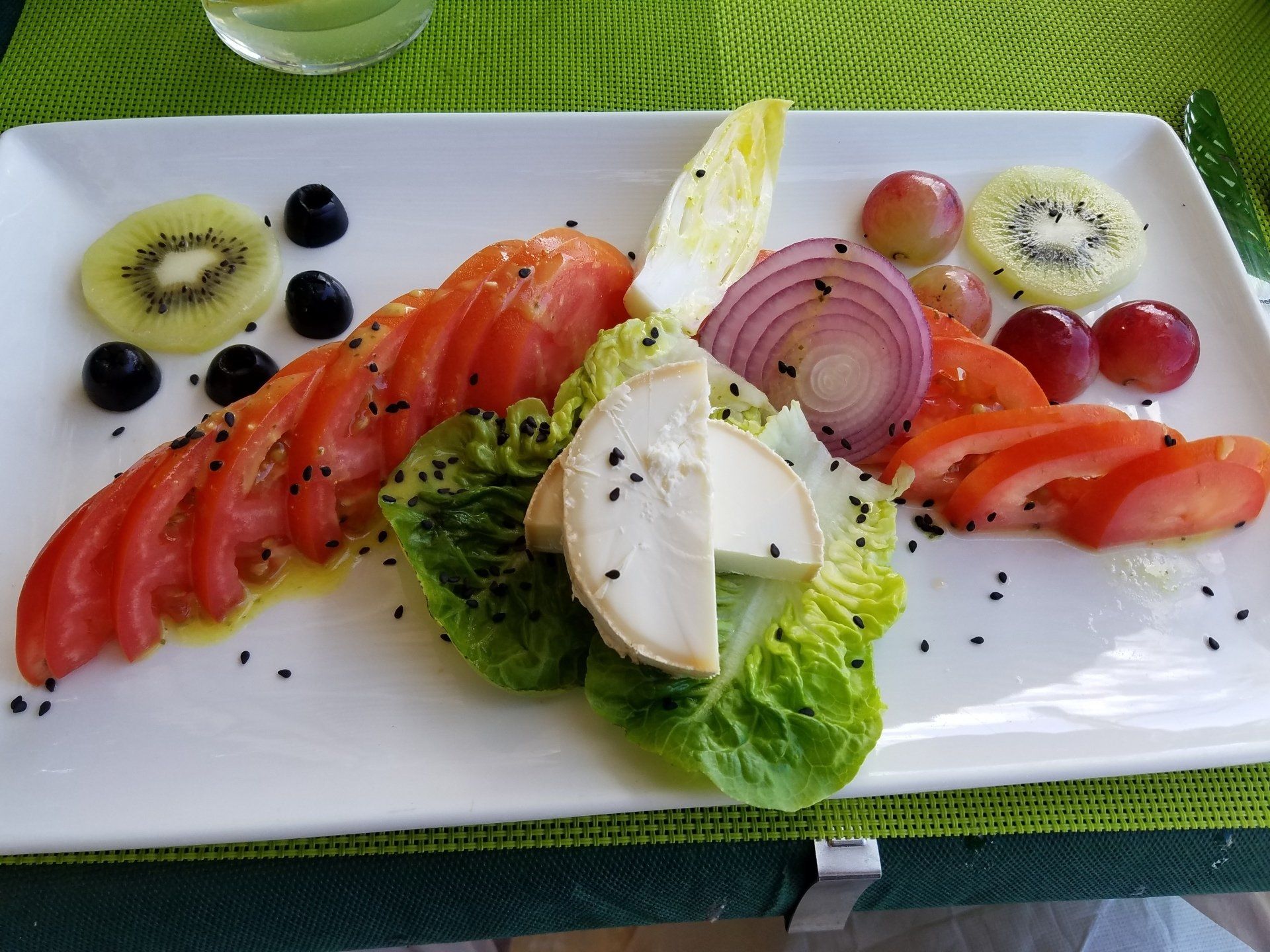 A white plate topped with sliced tomatoes , lettuce , grapes , onions and cheese.