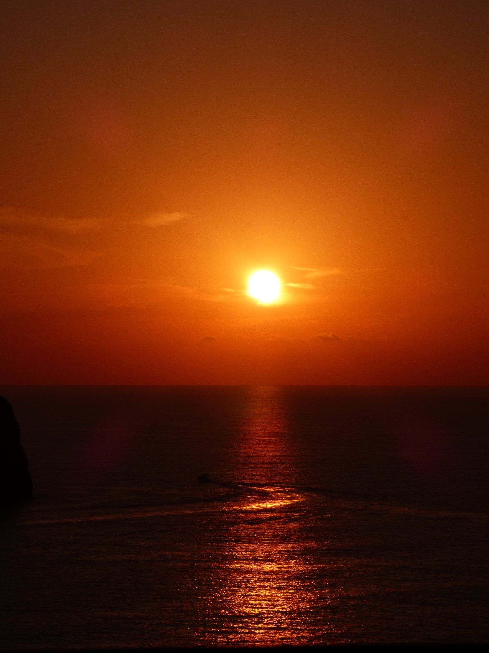 The sun is setting over the ocean with a boat in the distance.