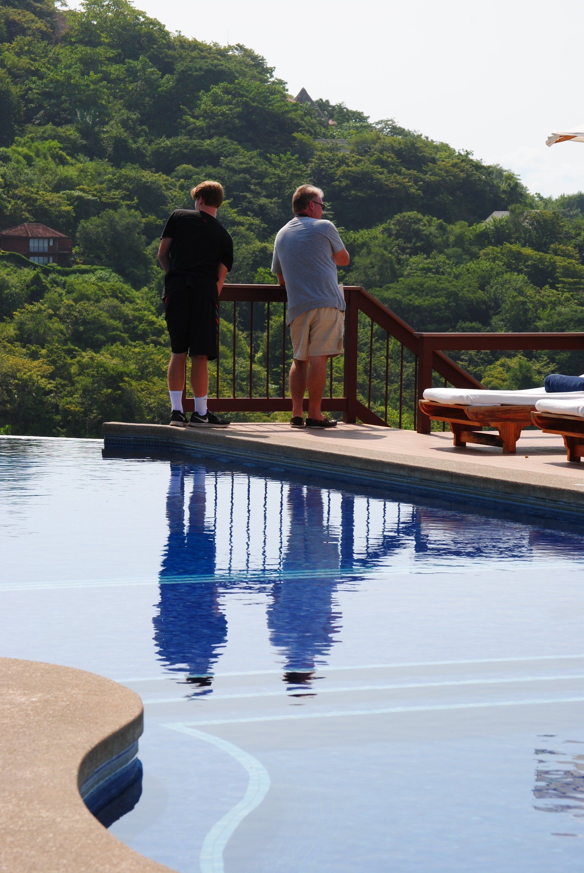Two men standing on a balcony overlooking an infinity pool