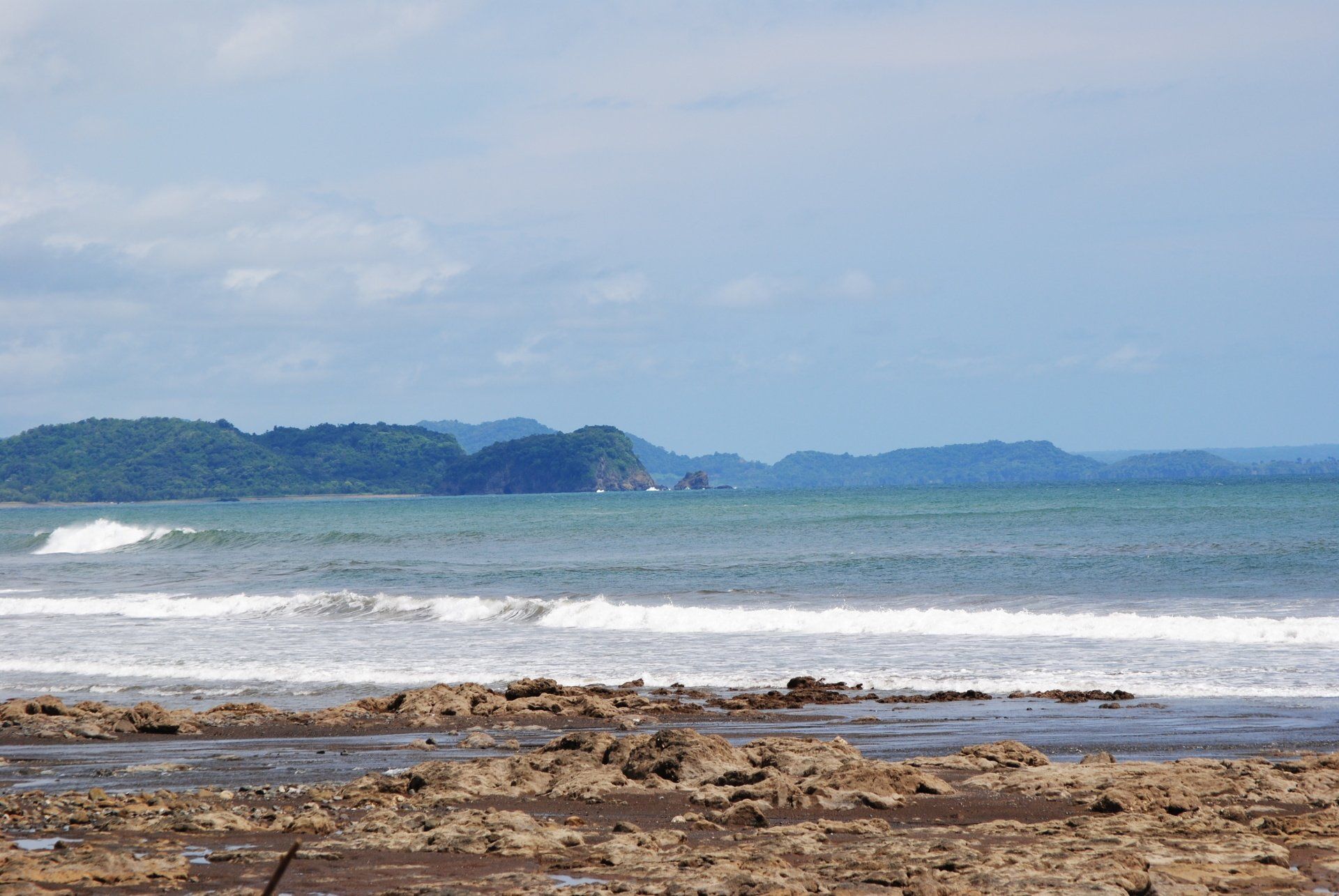 A beach with waves crashing on the rocks and mountains in the background