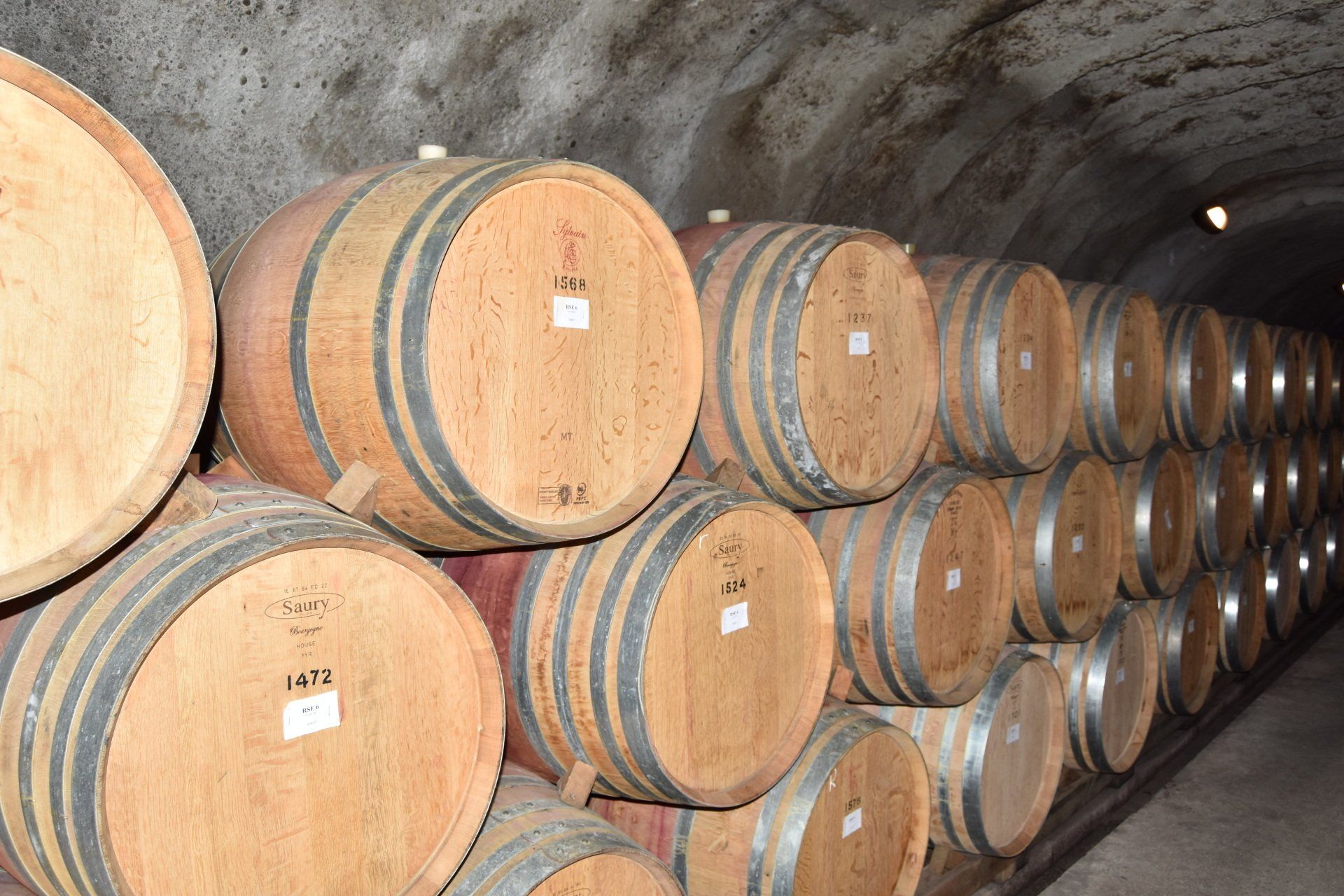 A row of wooden barrels are stacked on top of each other in a wine cellar.
