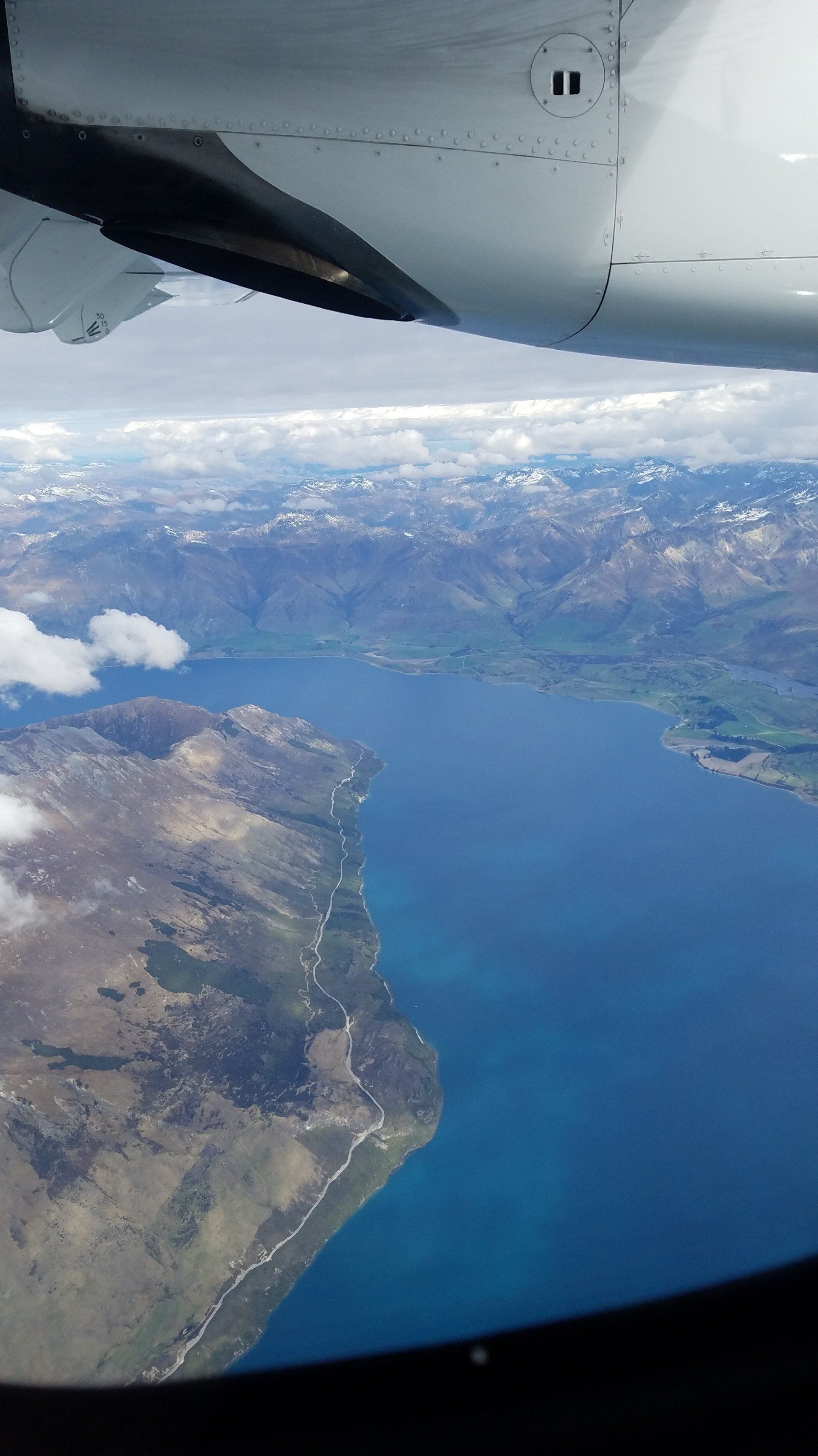 An aerial view of a lake and mountains from an airplane window.