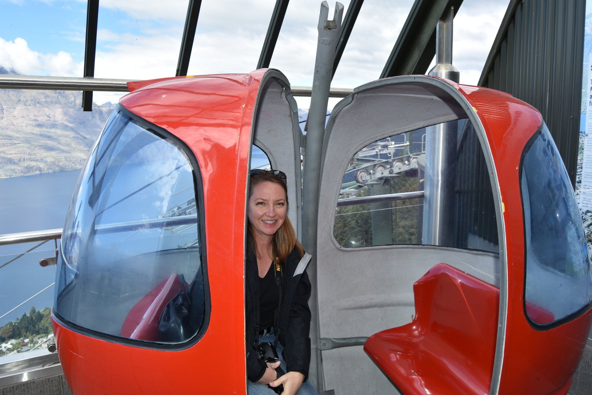 A woman is sitting in a red gondola overlooking a lake.