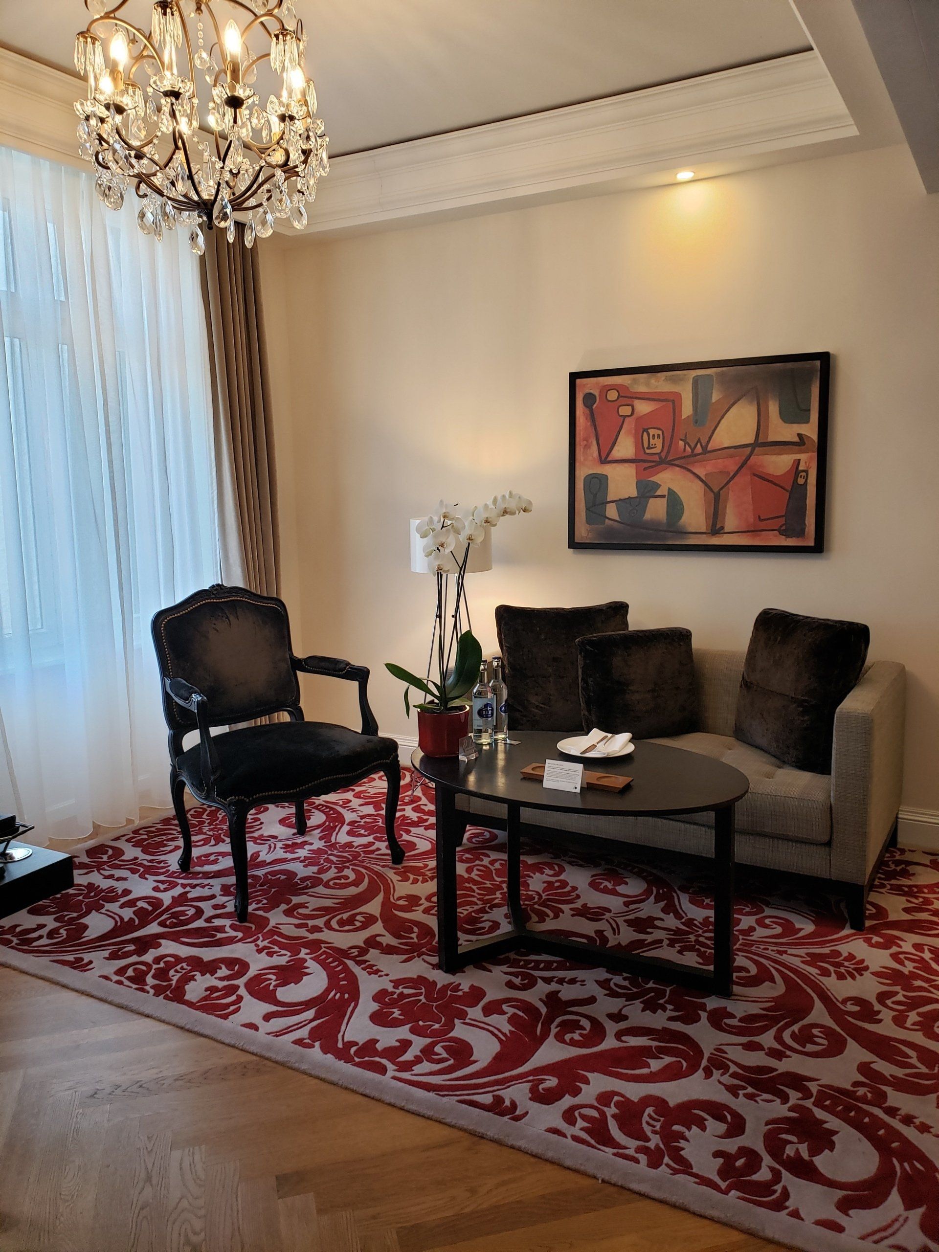 A living room with a couch , chair , table and chandelier.