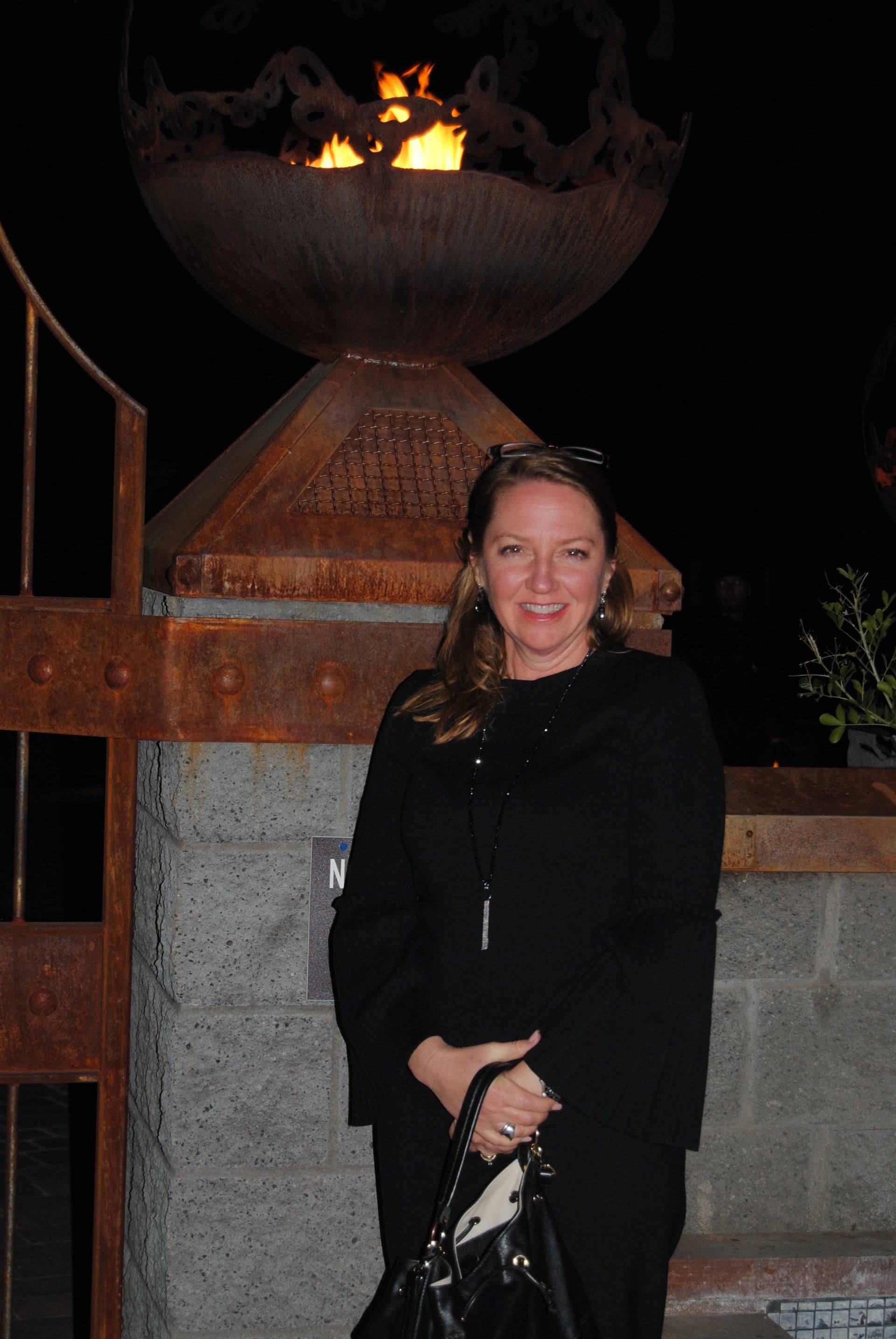 A woman in a black dress is standing in front of a fire pit