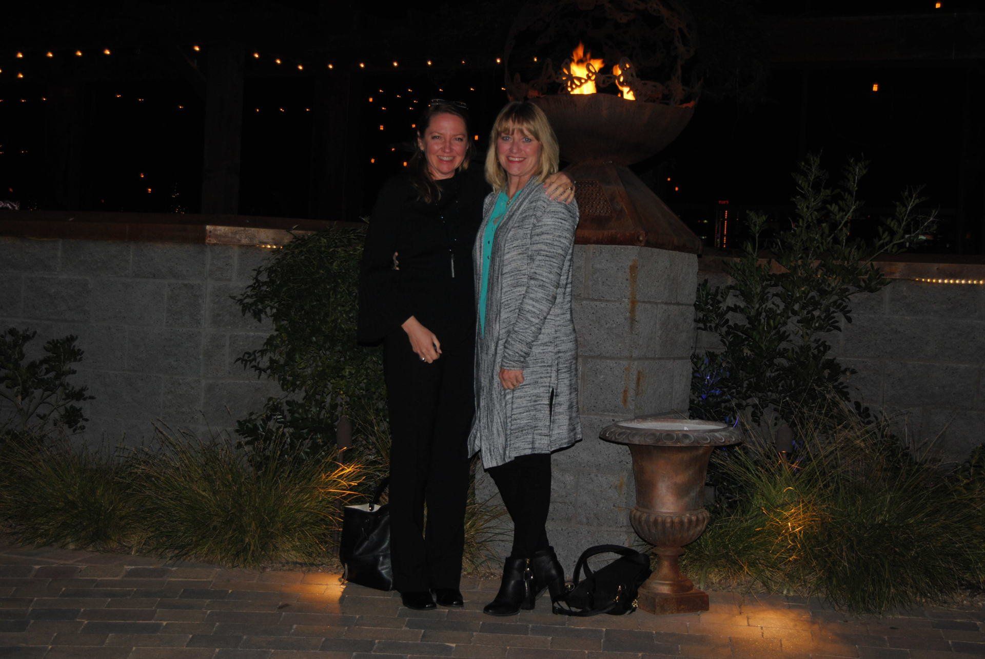 Two women are posing for a picture in front of a fire pit at night.