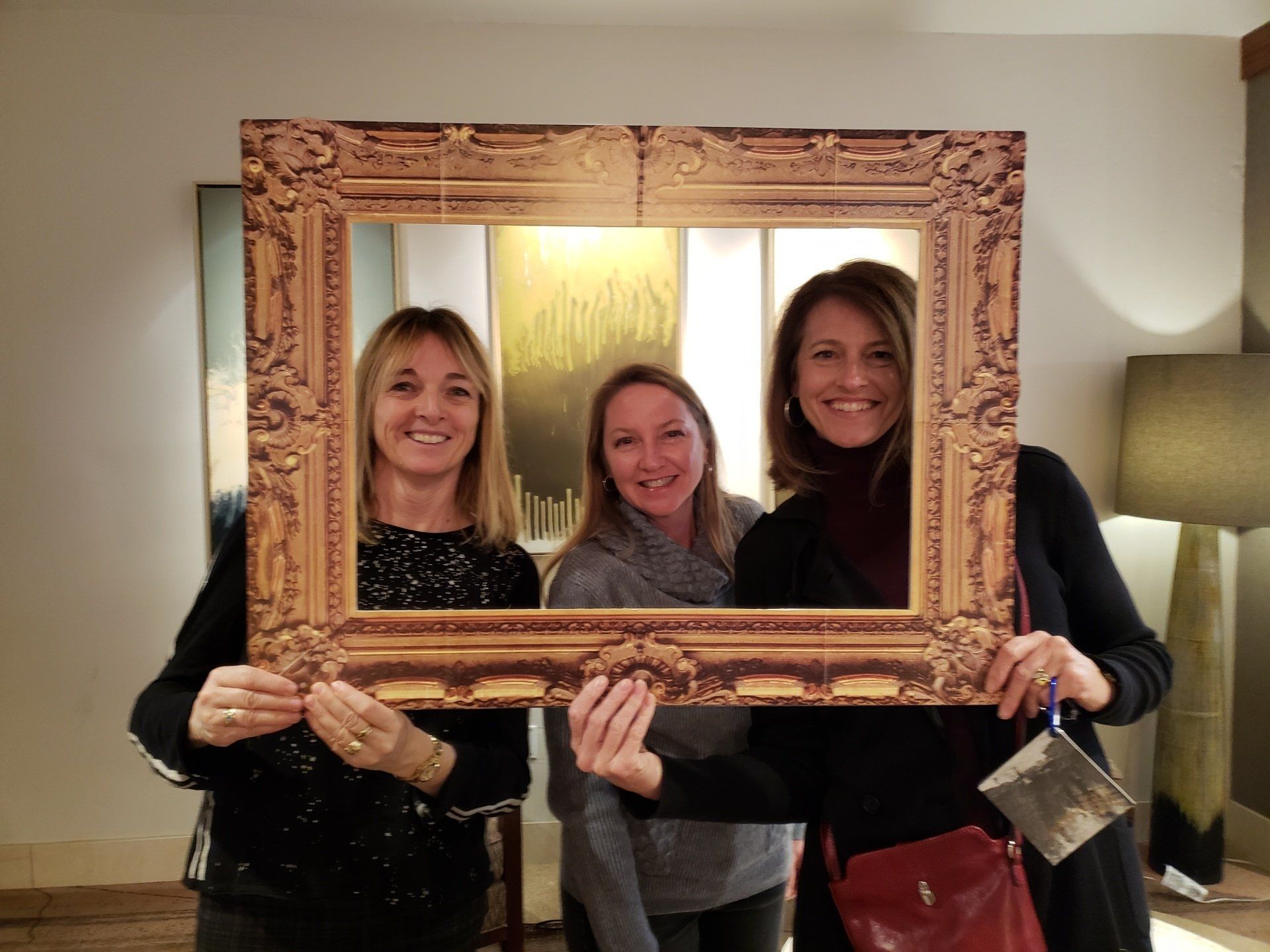 Three women are posing for a picture while holding a picture frame.