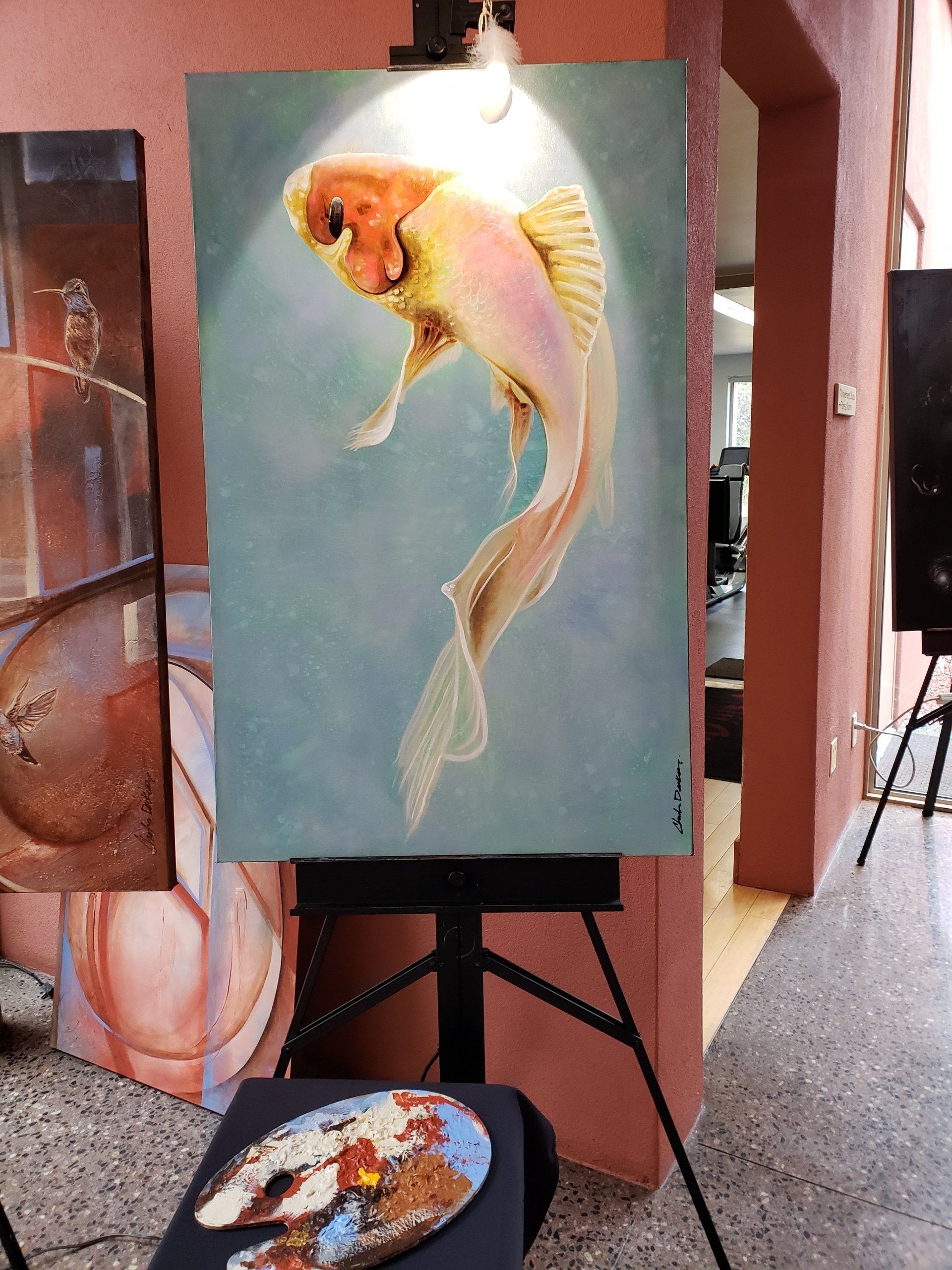 A painting of a fish on an easel next to a palette