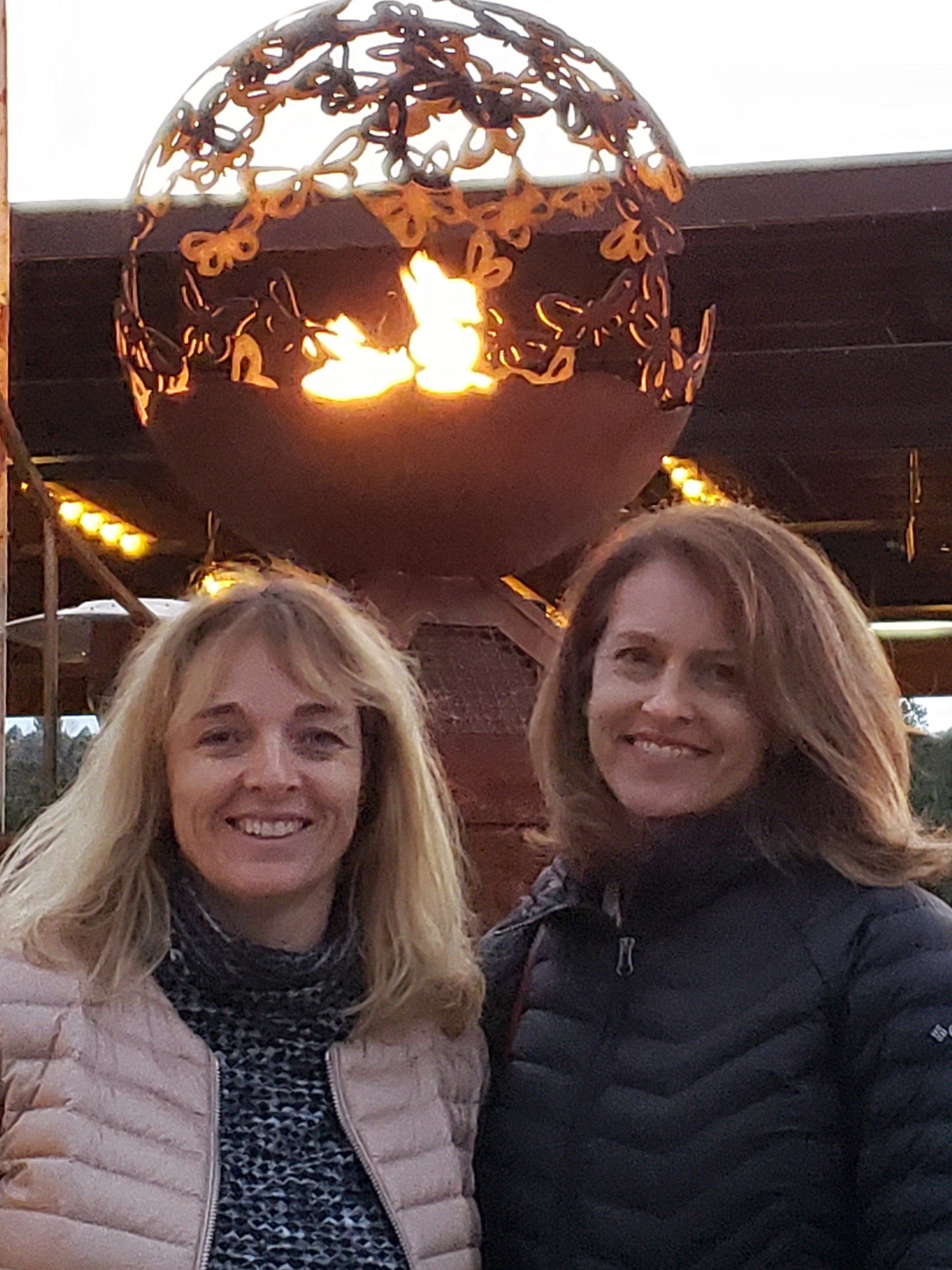 Two women are posing for a picture in front of a fire pit