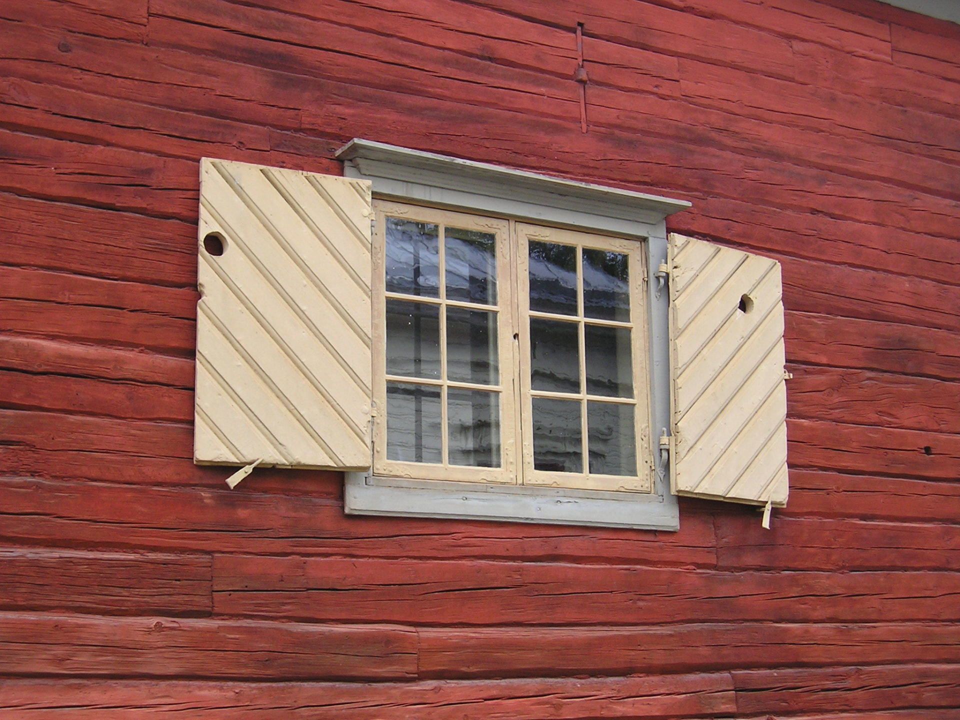 A window on a red wooden wall with the shutters open