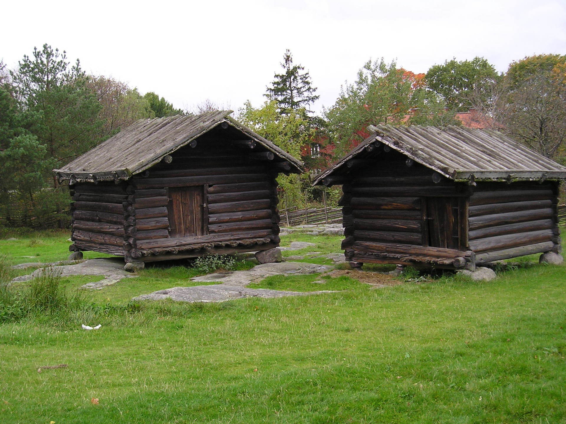 Two log cabins in a grassy field with trees in the background