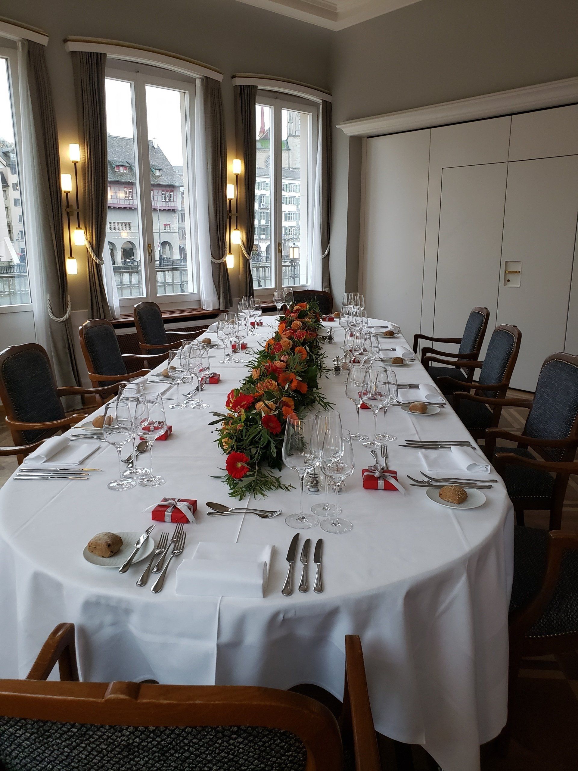 A long table with a white tablecloth and flowers on it in a room with chairs.