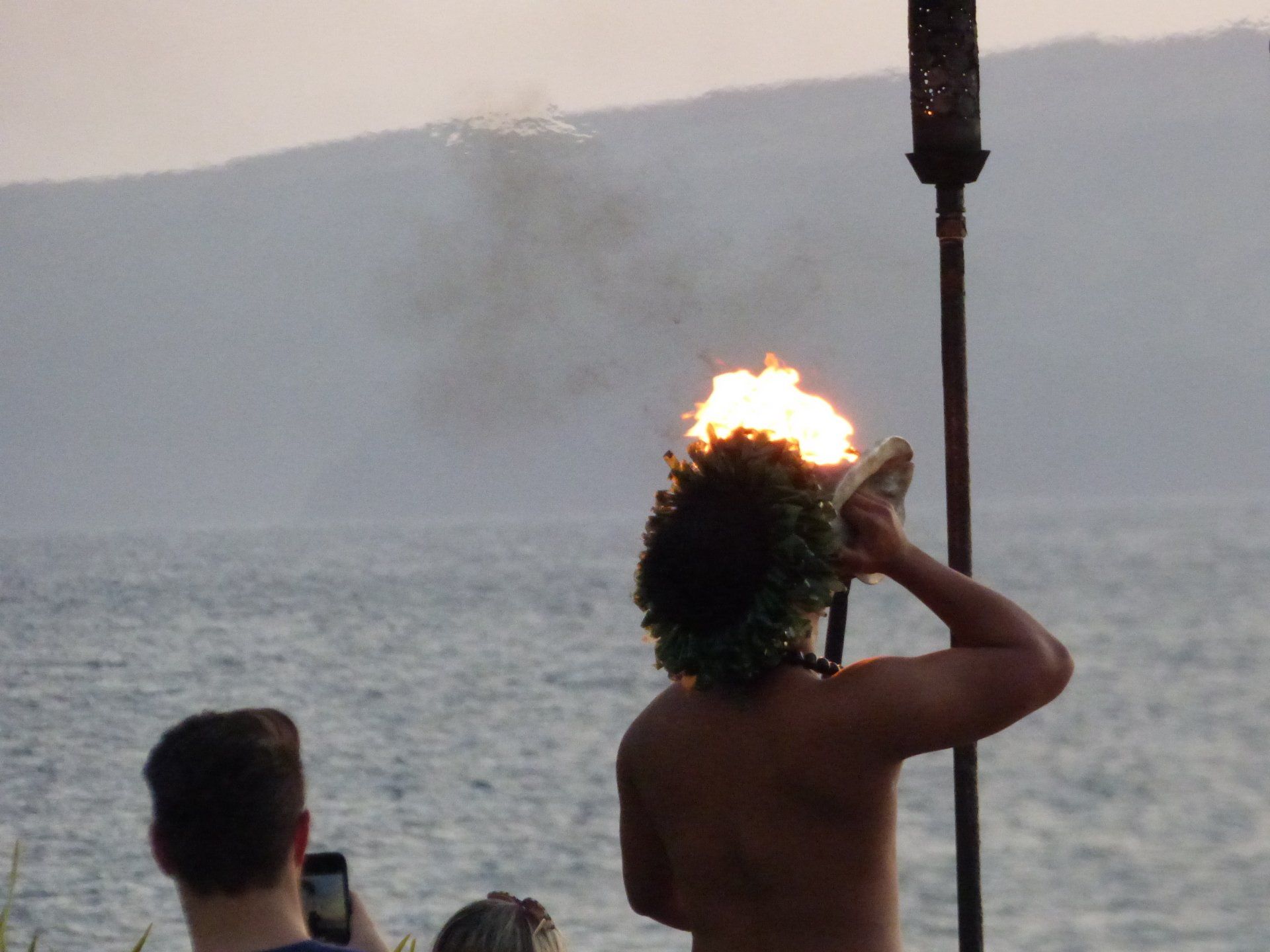 A man is holding a torch in front of the ocean