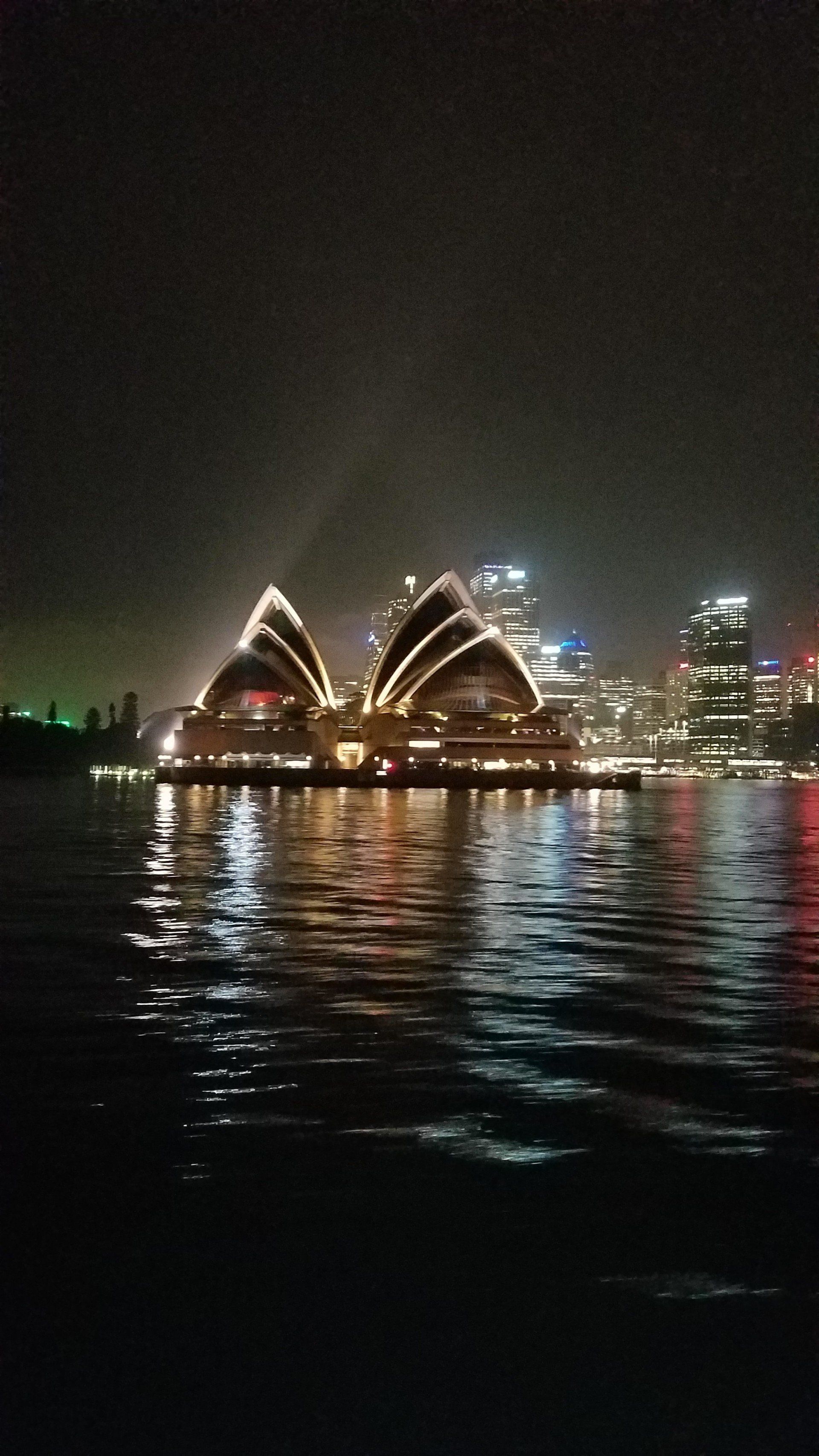 The sydney opera house is lit up at night and reflected in the water.