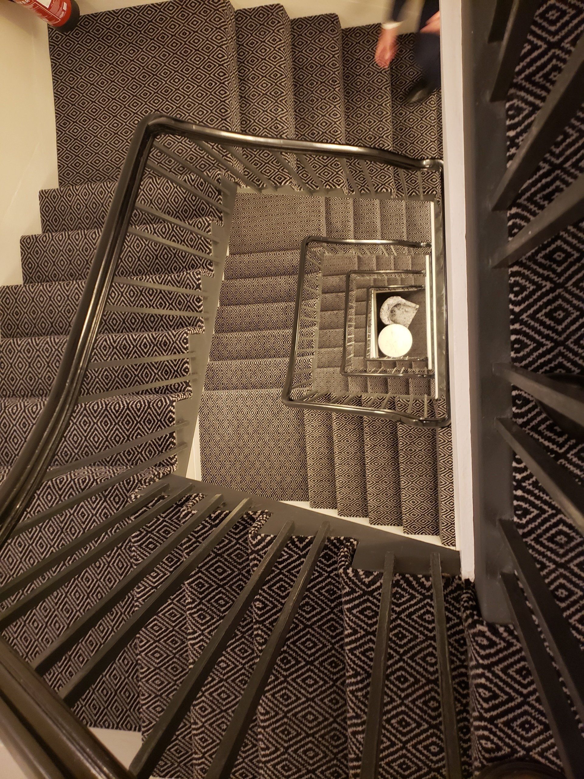 A person is walking down a spiral staircase with a black railing.