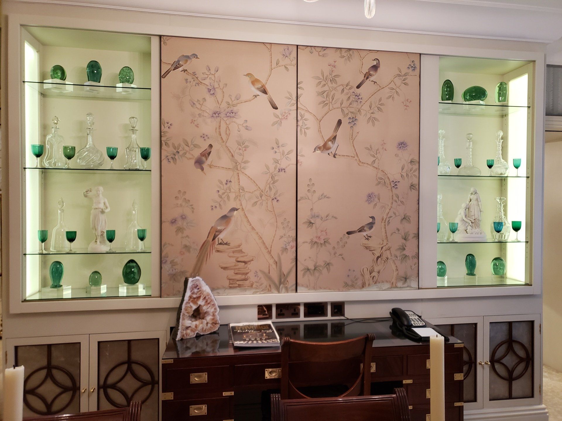 A room with a desk and shelves and a wall with birds on it