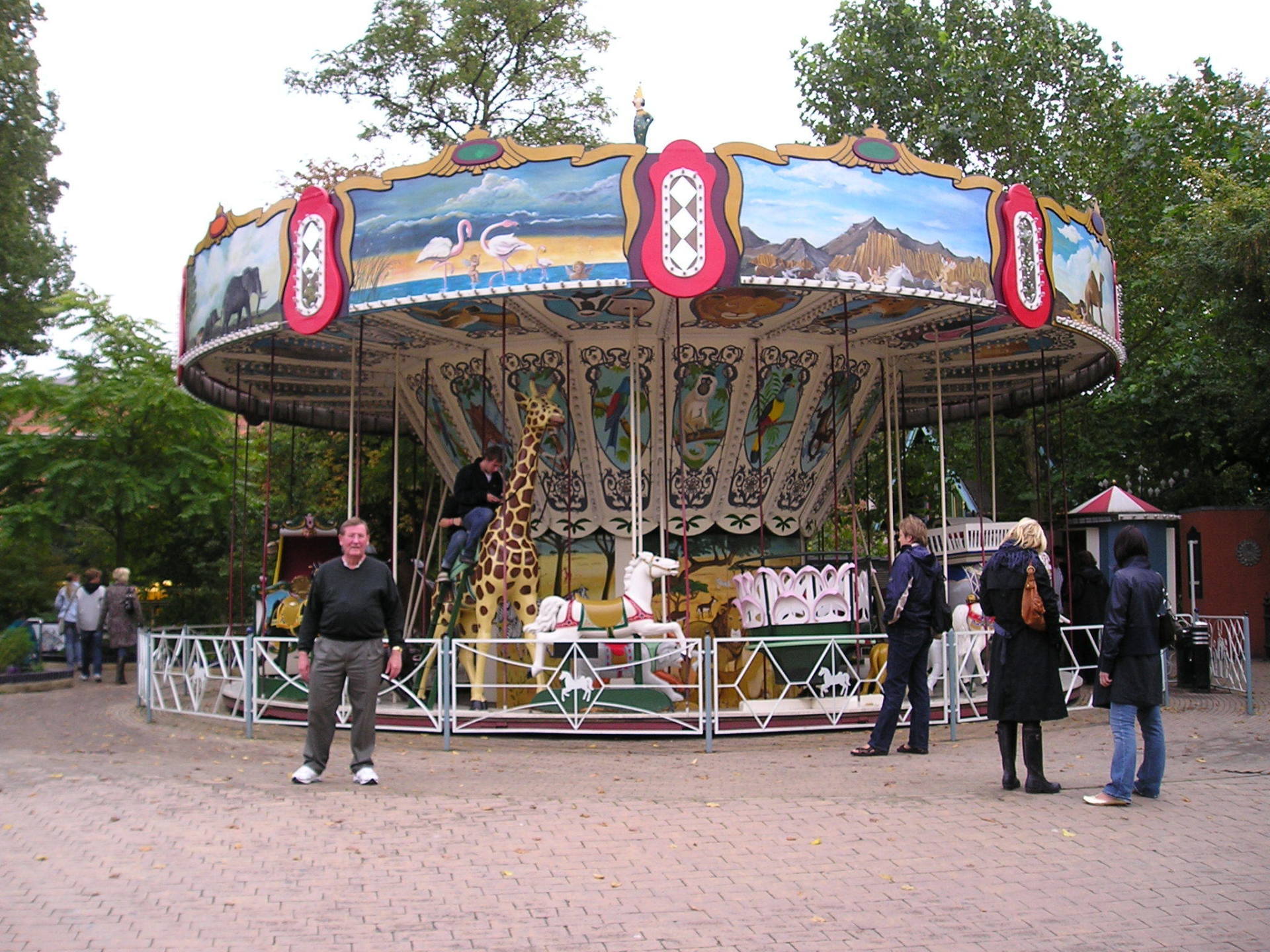 People standing around a merry go round with a giraffe on it