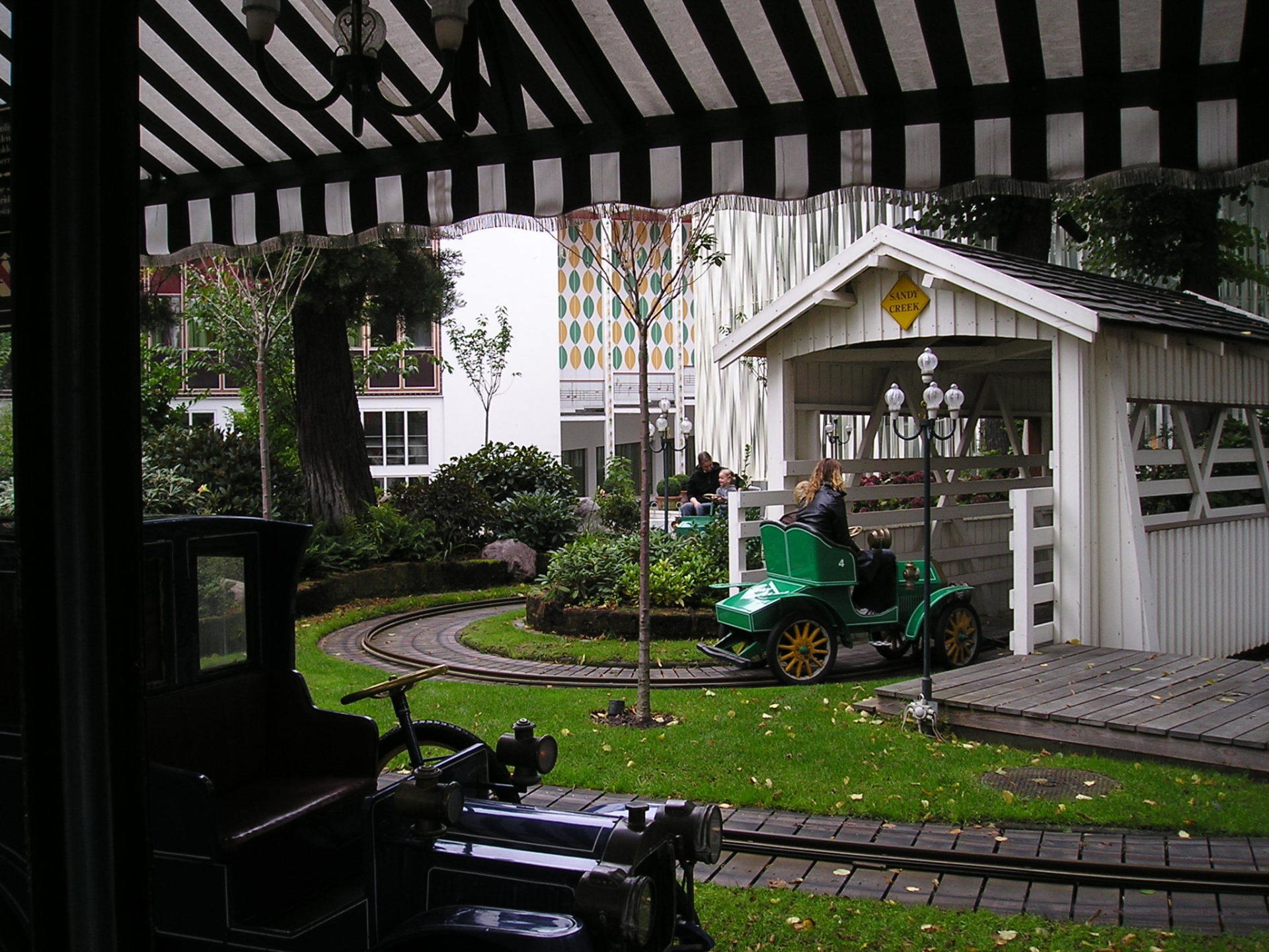 A green car is driving under a covered bridge