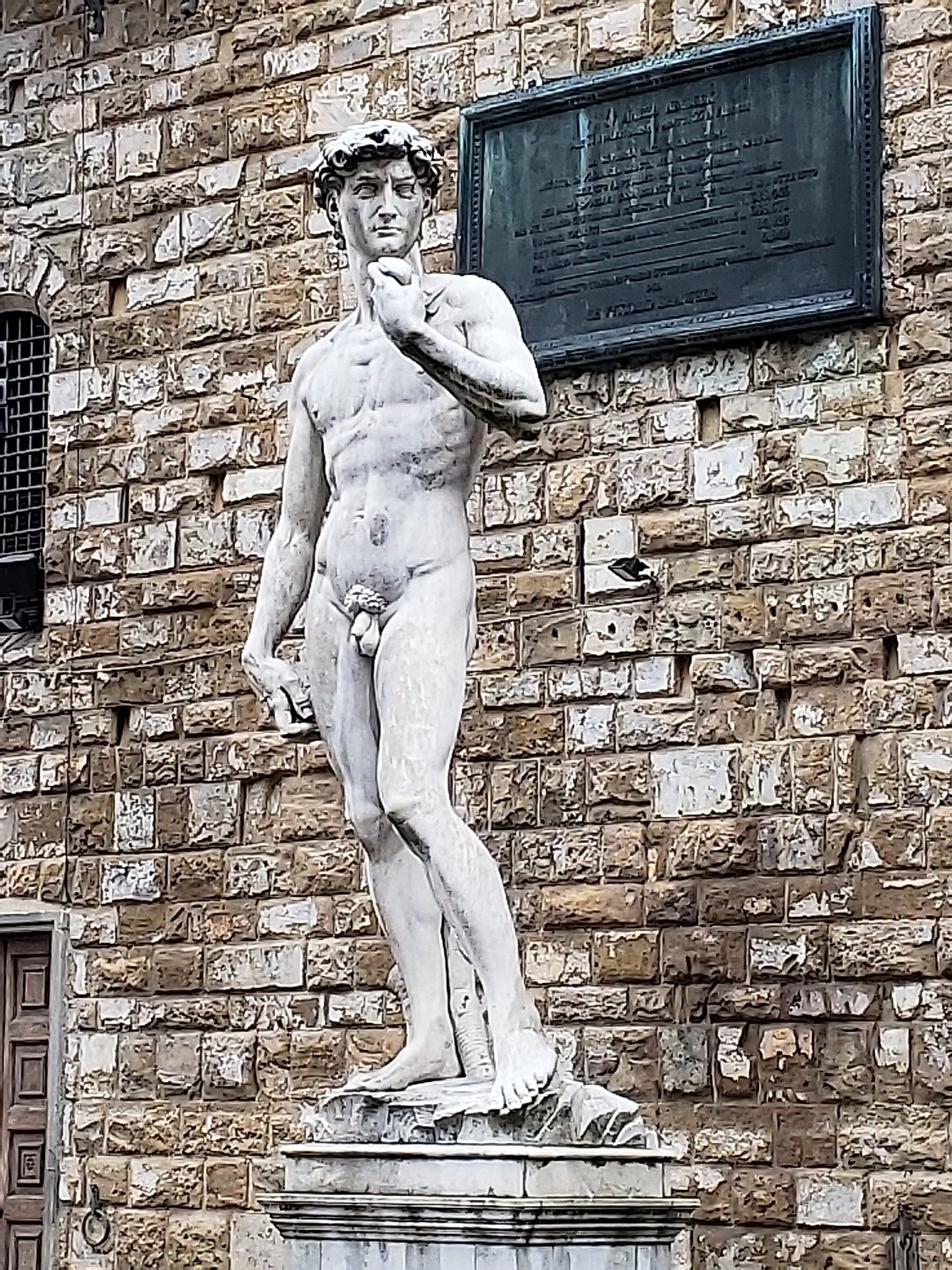 A statue of a man standing in front of a brick wall.