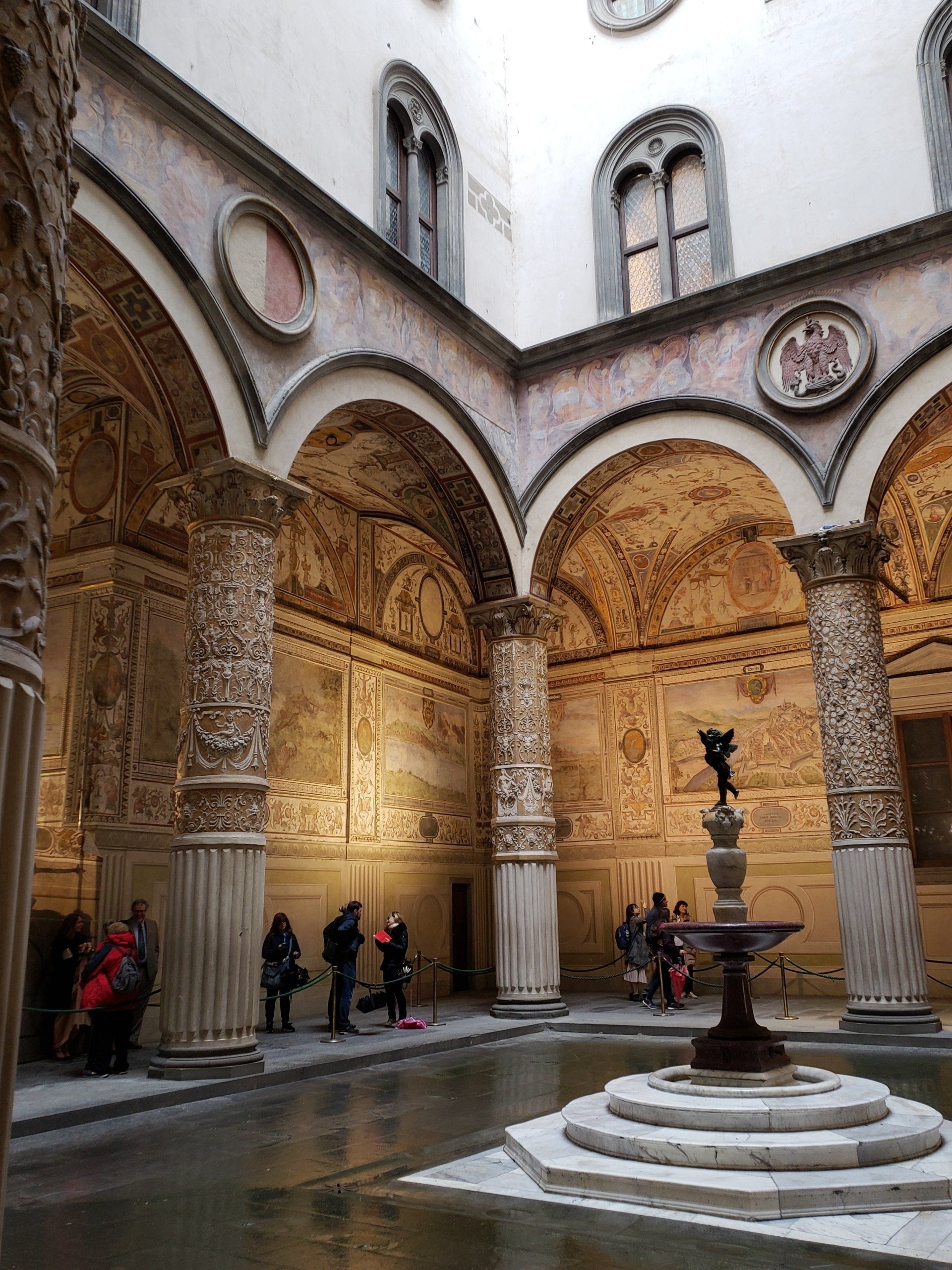 A courtyard with arches and columns and a fountain in the middle