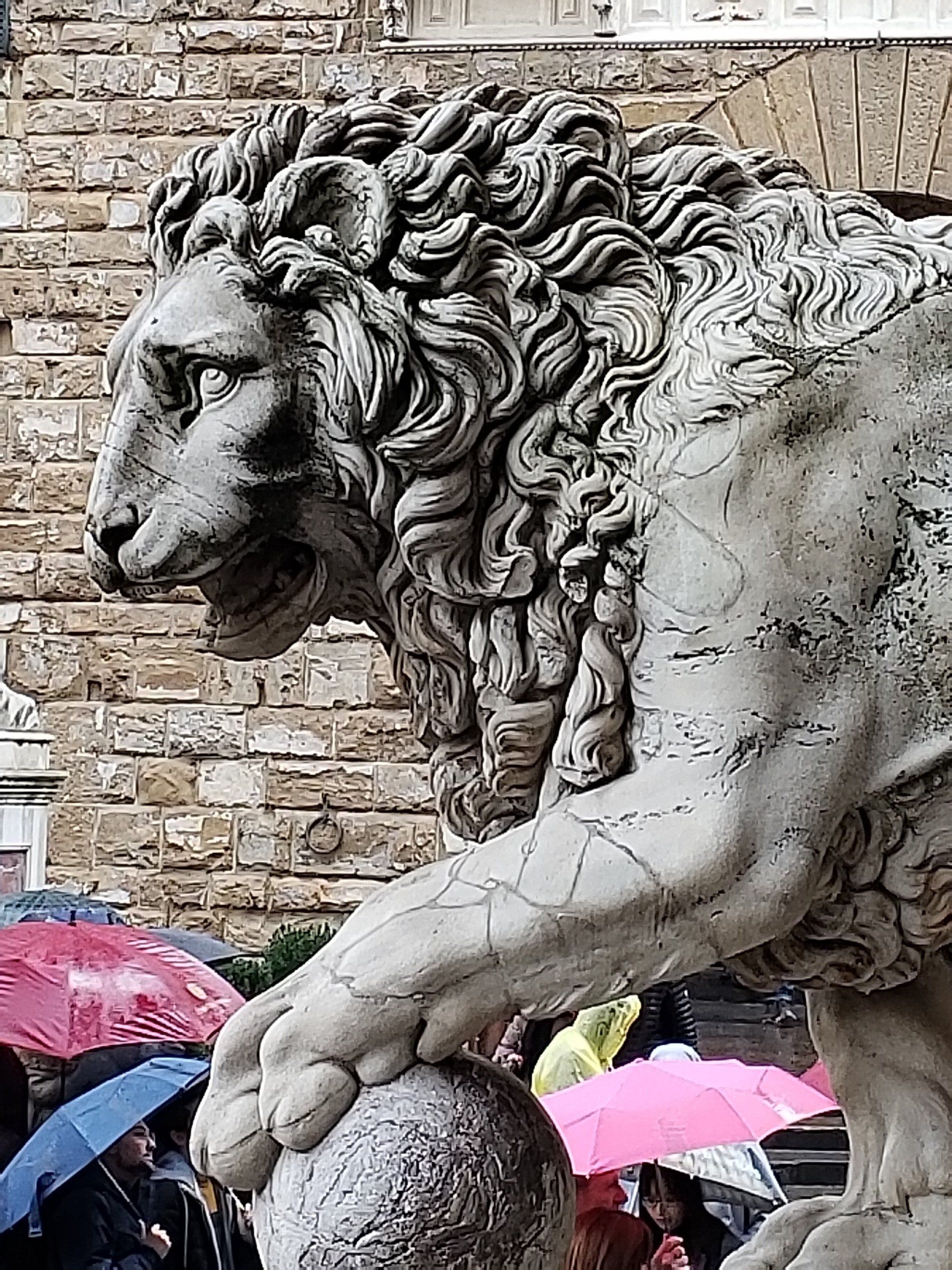 A statue of a lion is standing on a rock in front of a brick building.