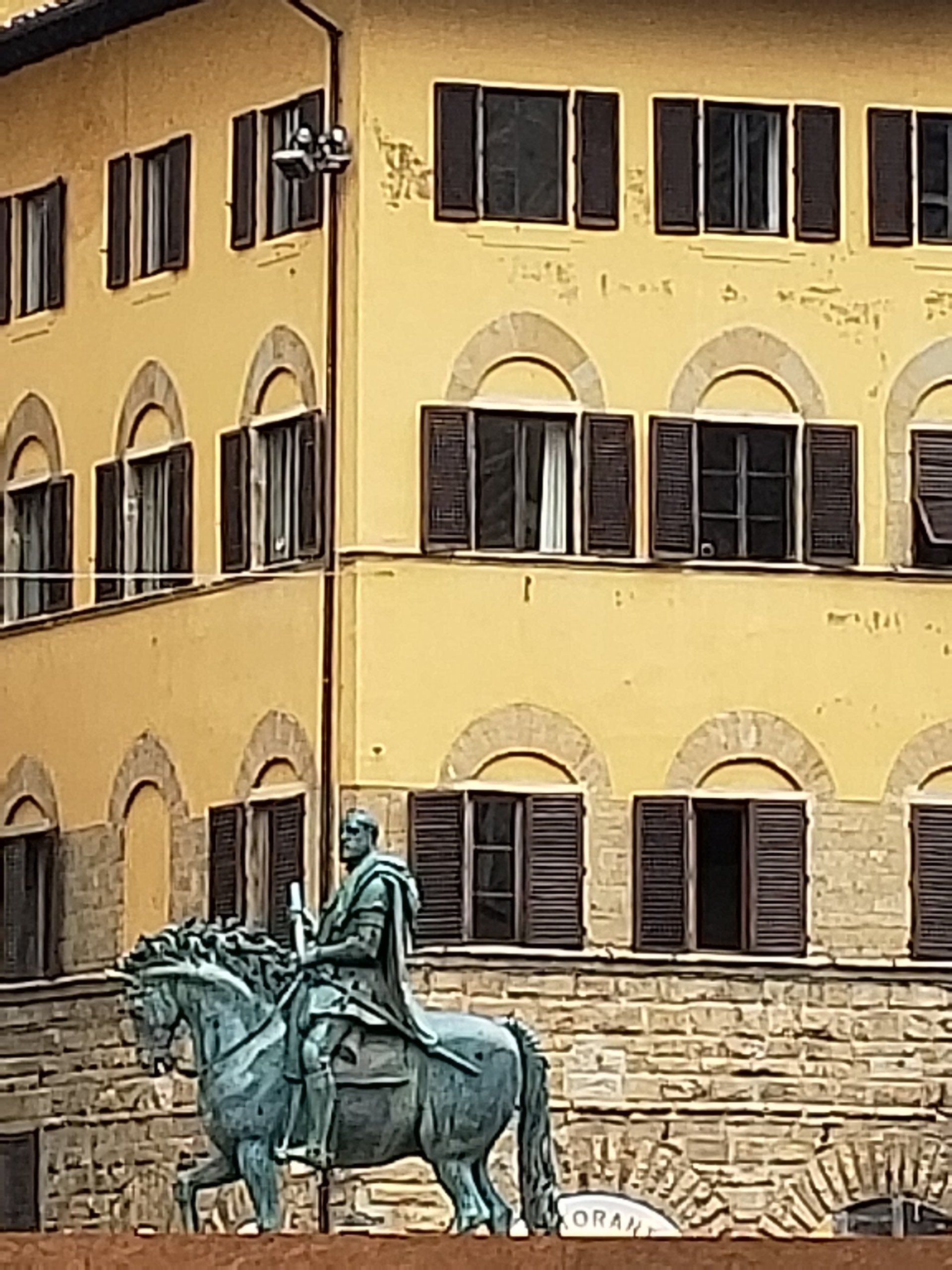 A statue of a man riding a horse in front of a yellow building.