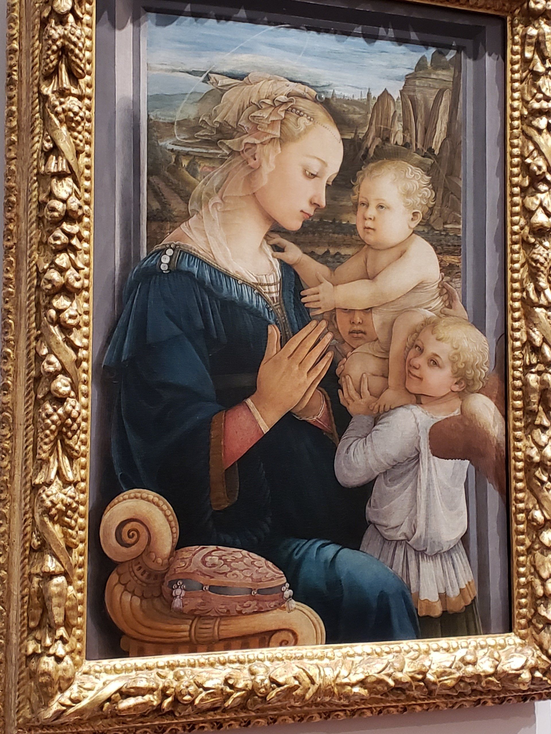 A painting of a woman holding two children in a gold frame