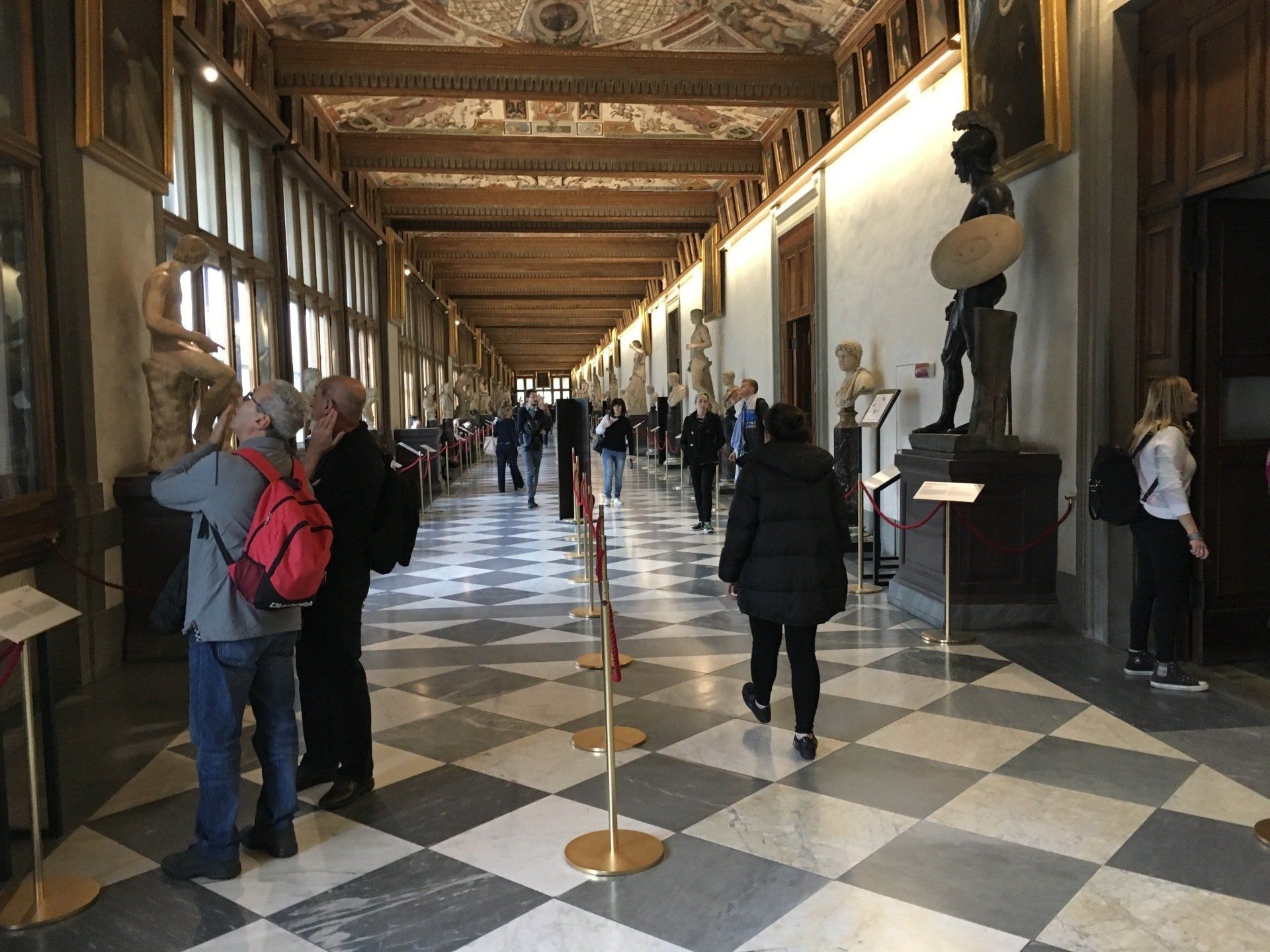 A group of people are walking down a long hallway in a museum.