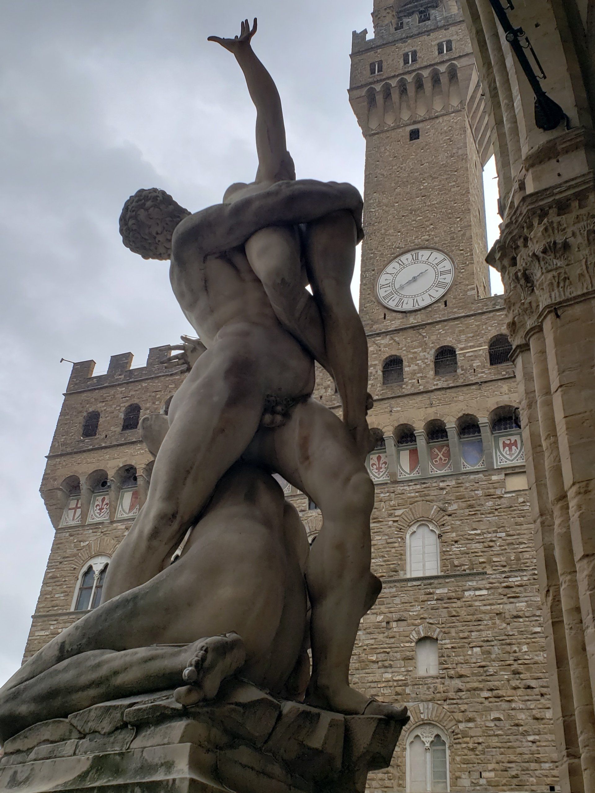 A statue of a man carrying another man in front of a clock tower