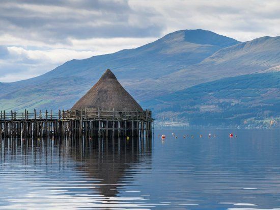 A small hut on a pier in the middle of a lake with mountains in the background.