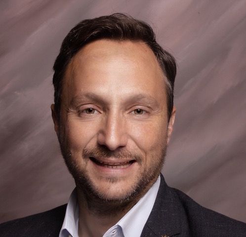 A man in a suit and white shirt is smiling for the camera.