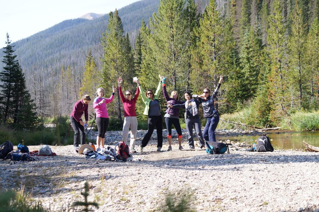 A group of people are standing in front of a river with their arms in the air.