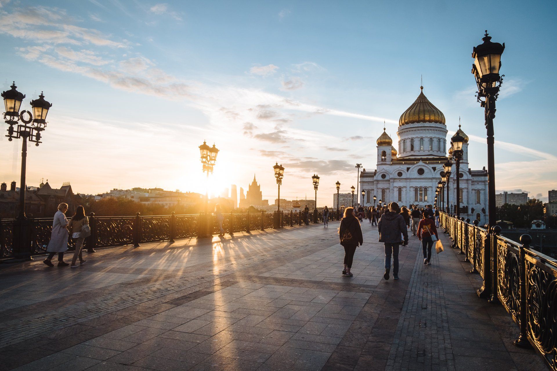 A group of people are walking across a bridge in front of a large building at sunset.