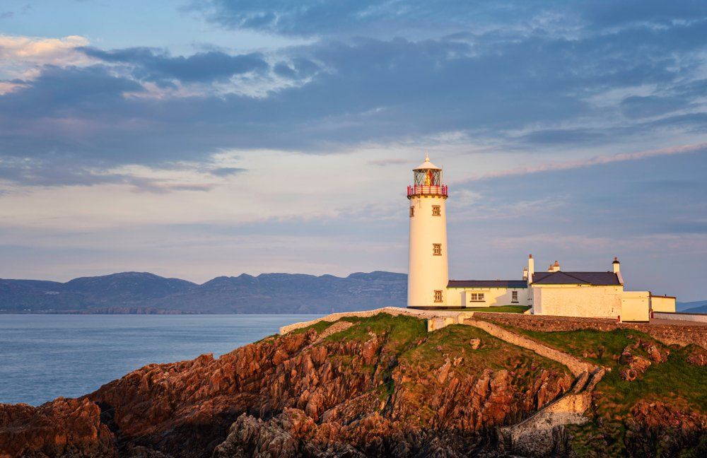 A lighthouse is sitting on top of a rocky hill overlooking the ocean.