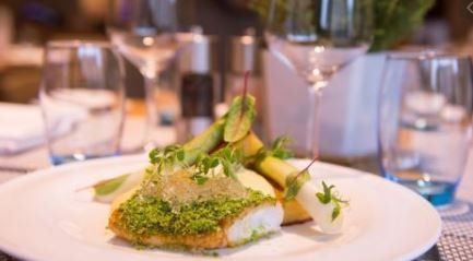 A close up of a plate of food on a table with wine glasses in the background.