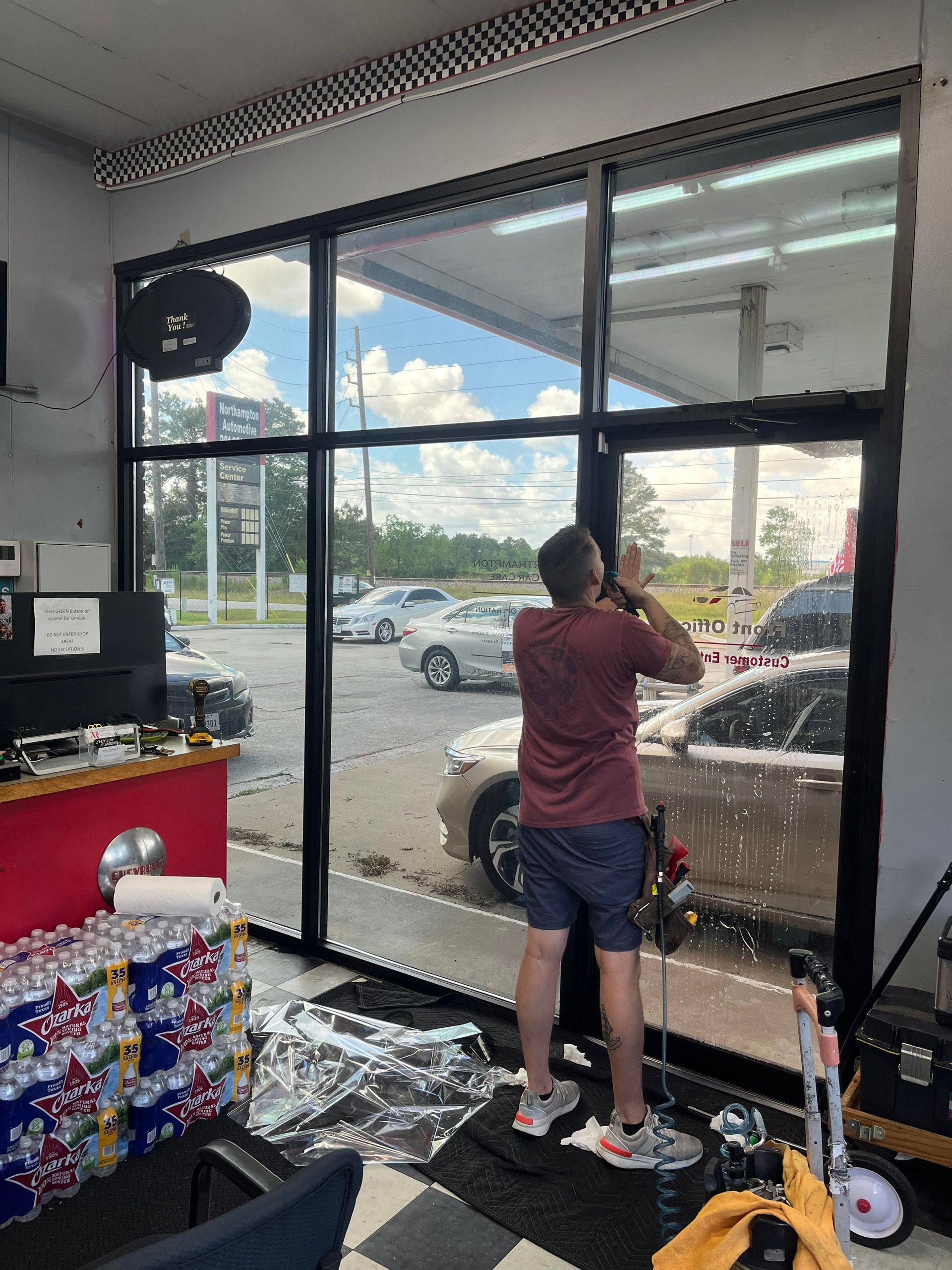 Man installing window tint in a shop; exterior view with cars.