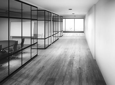 Office hallway with glass-walled conference rooms, wood floor, and large windows at the end.