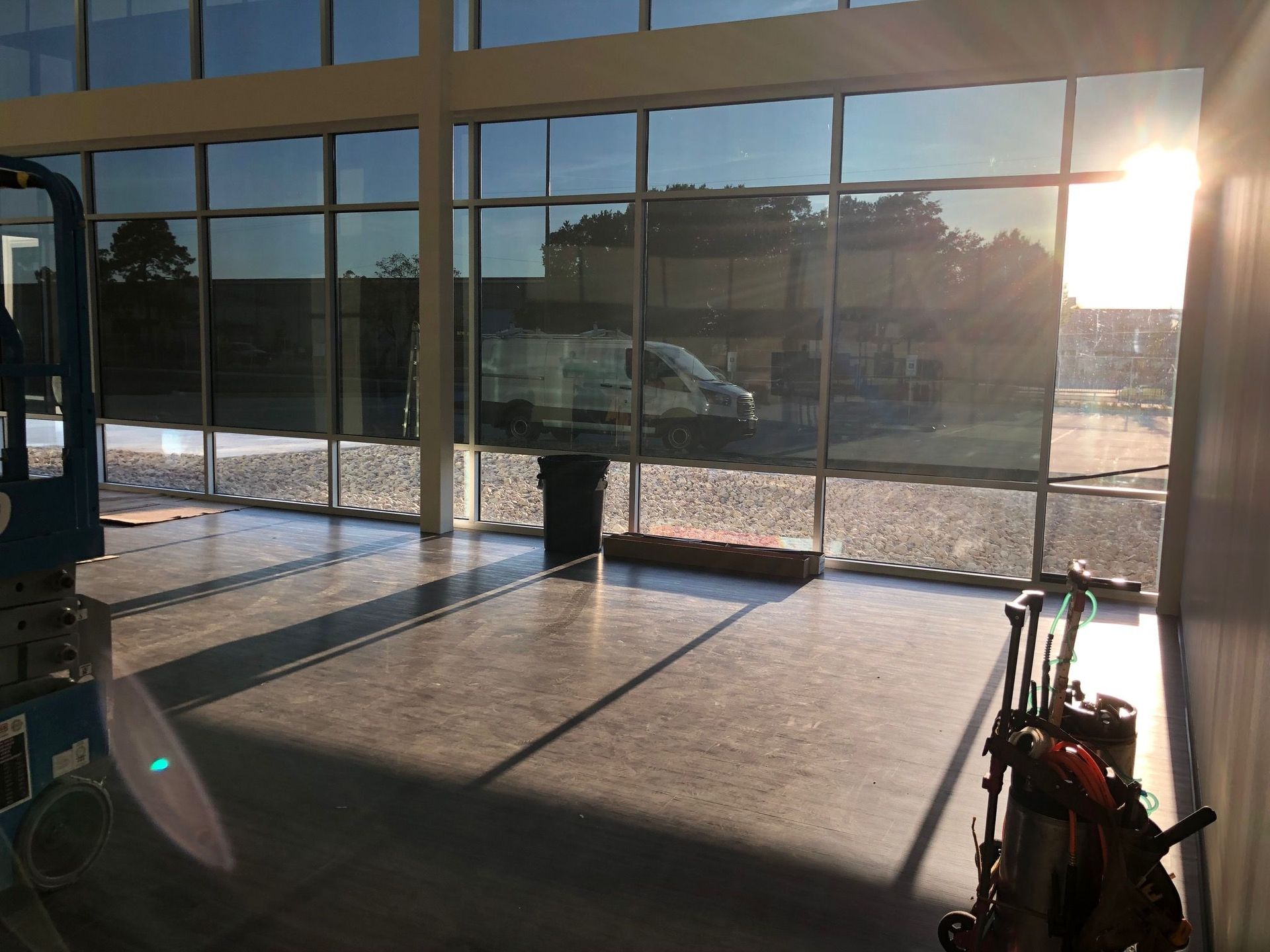 Interior view of a modern building with large tinted windows. Sunlight casts shadows on the concrete floor.